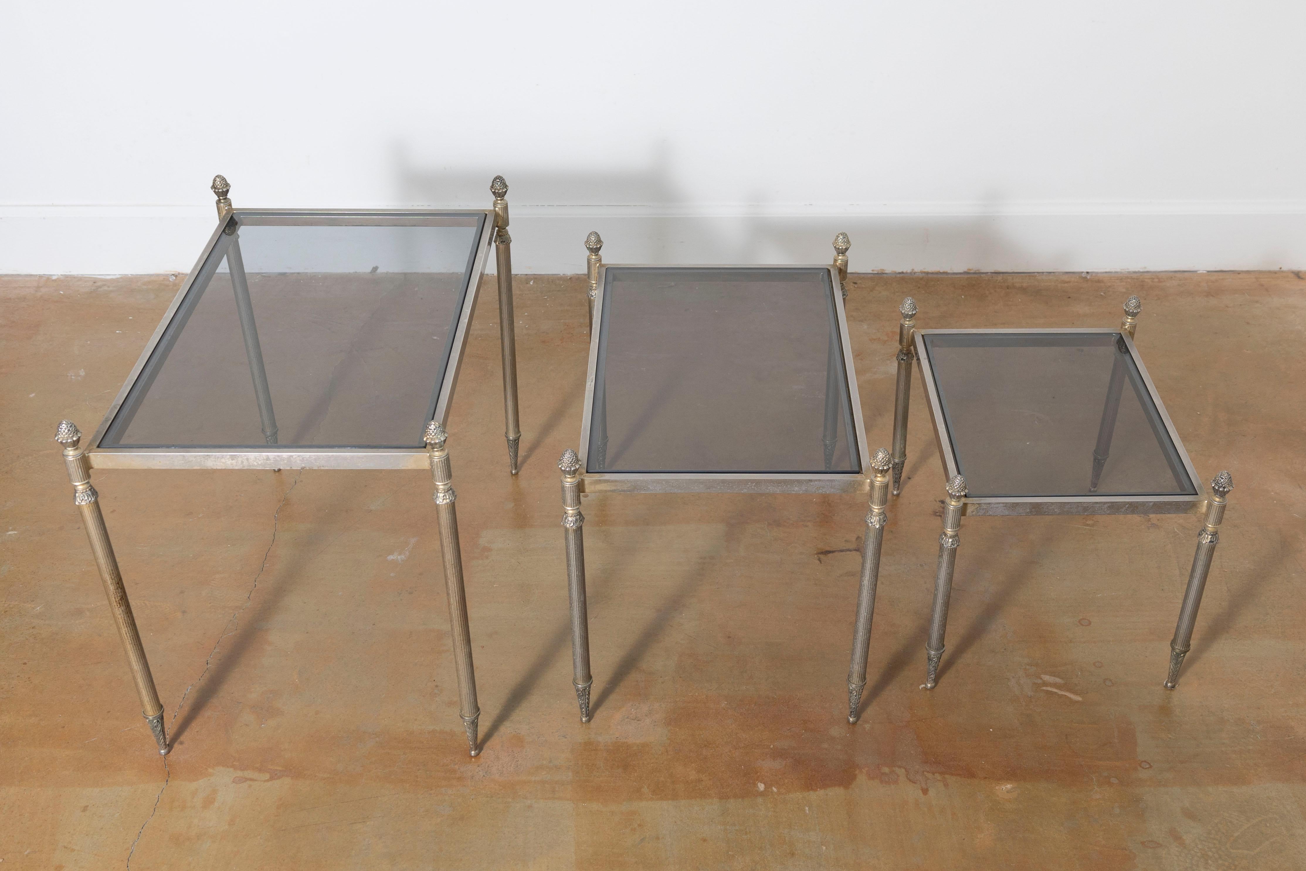 This 20th-century French set of three nesting tables embodies elegance and versatility, making them a functional and stylish addition to any interior. Crafted with gilded metal frames, these tables feature fluted legs adorned with detailed acanthus