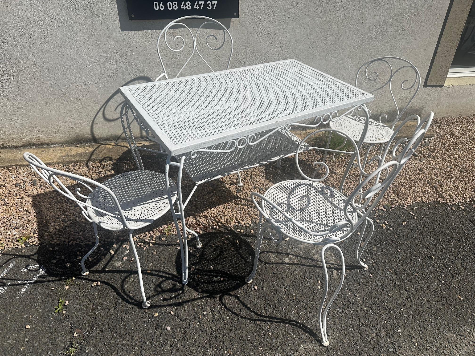Very nice white wrought iron garden set consisting of a rectangular table and four chairs. The table top is fully perforated, it also has a shelf under the top. This table could therefore be used as a console. 
Two small chairs with also perforated