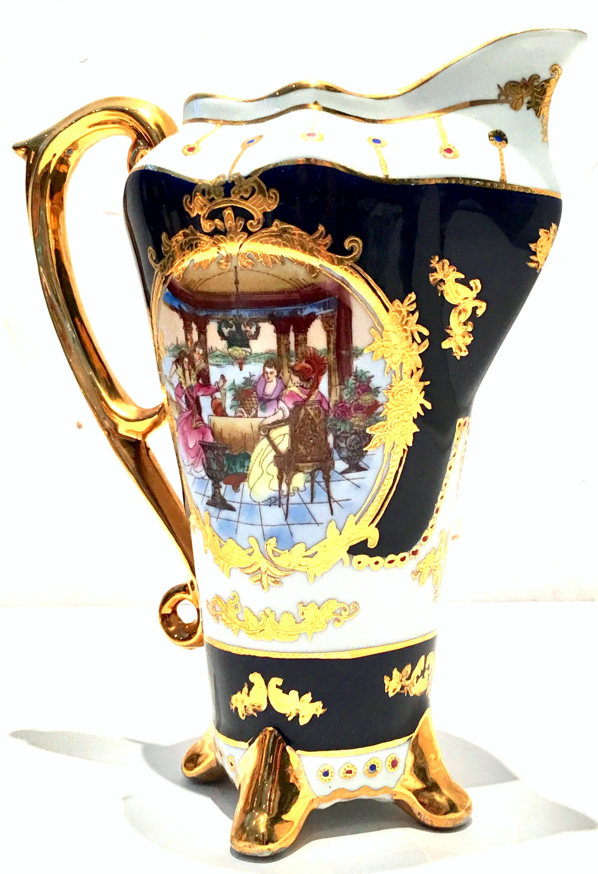 Mid-Century porcelain Limoges Style cobalt & 22-karat gold pitcher. This ornate and heavily gilded and decorated French Sevres style porcelain handled pitcher features a bright white ground with cobalt blue, two sided 18th century group of diners