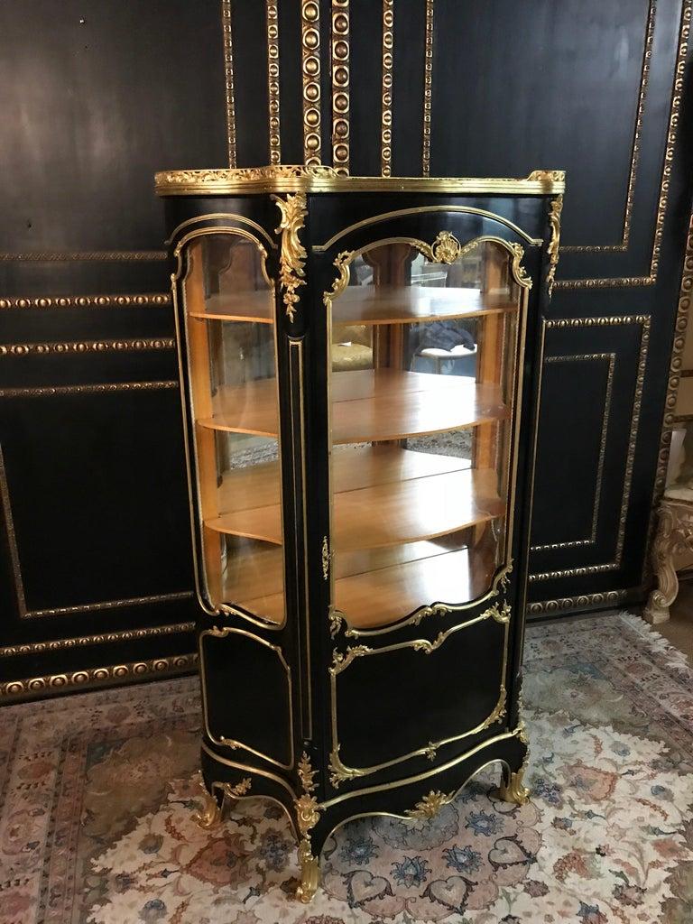French cabinet according to Paul Sormani in transition style.
Piano black polished veneer on solid beech. High-rectangular, one-armed, cambered and three-sided glazed corpus on high, slanting, curly feet in sabots. Three-sided scalloped, cambered,