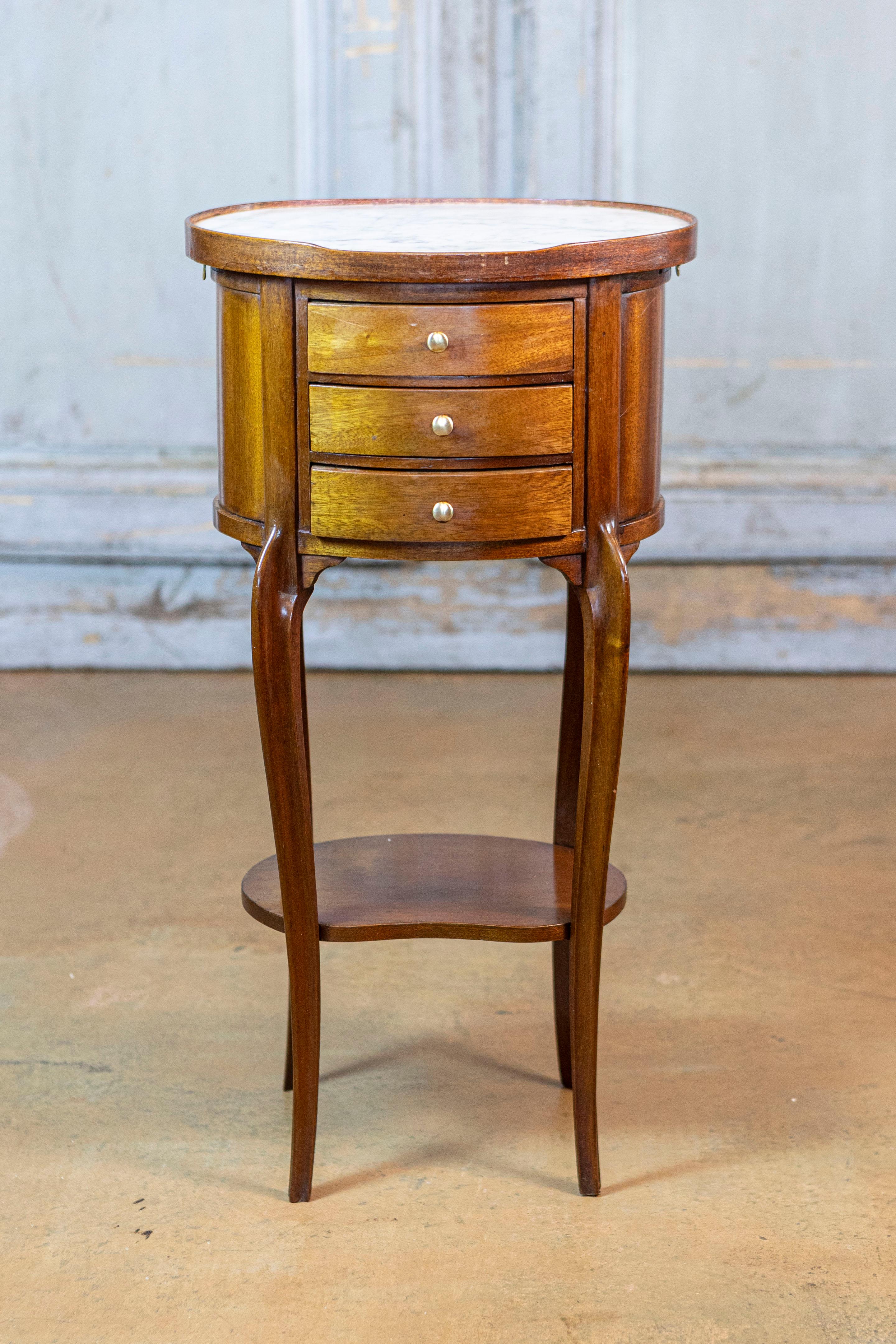 This elegant 20th-century mahogany chiffonier table combines functionality with refined craftsmanship. The piece features a rounded body that opens with three drawers on the front, each adorned with brass buttons, and two discreet pull-outs on