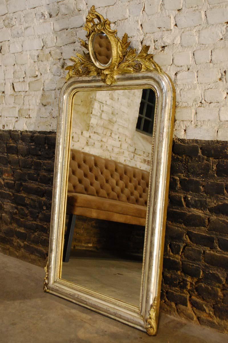 This beautiful mirror is partially silver leaf gilt. It has remnants of gold paint and it shows the bone color of the gesso. 
This mirror was originally a “gold” mirror. It’s golden appearance was made by the use of gold paint (gold dust mixed with