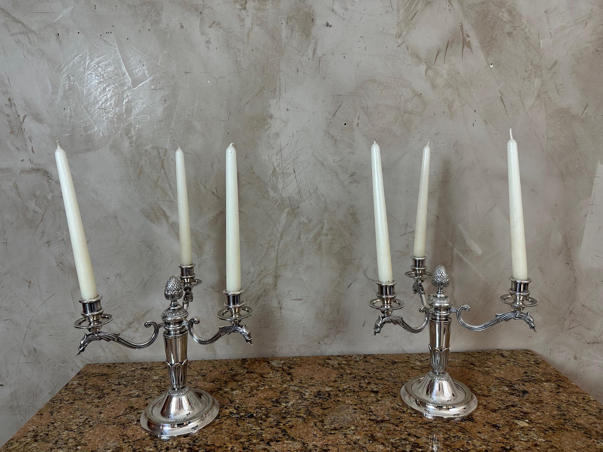 Magnífico par de candelabros de tres brazos bañados en plata, finamente elaborados en un estilo clásico y refinado.
Cada candelabro presenta una esbelta columna adornada con delicados motivos de follaje y rematada con un fino detalle de piñas,