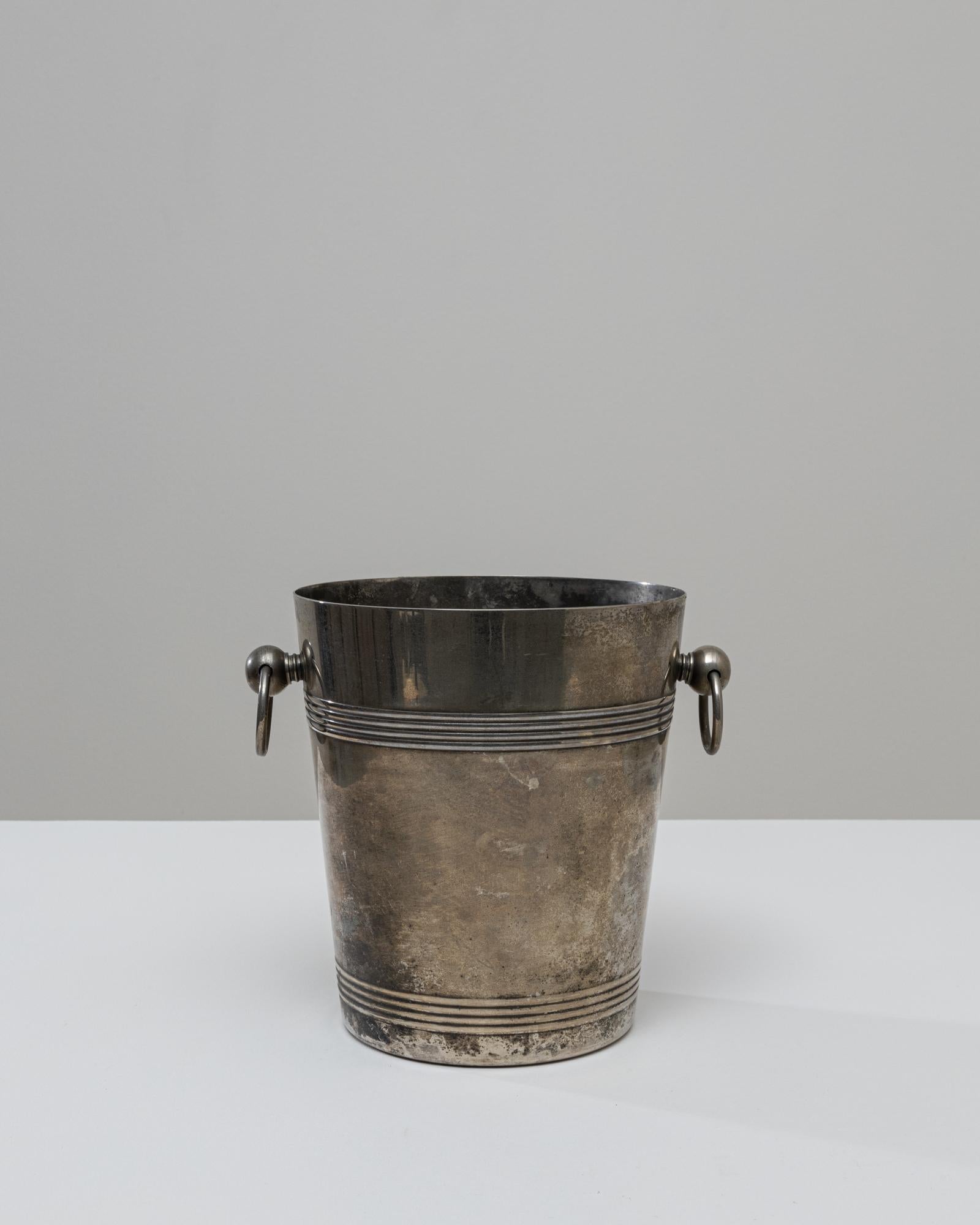 Un seau à champagne en métal argenté français du 20e siècle qui se distingue par son élégance discrète et sa surface magnifiquement vieillie. La forme cylindrique est rehaussée d'un triple anneau en haut et à la base, ce qui ajoute une texture
