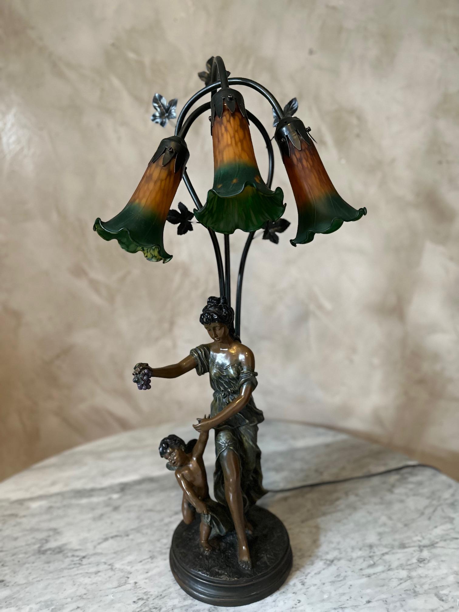Beautiful and large spelter lamp representing a young woman and a cherub. The woman holds a bunch of grapes in her right hand. 
Behind her, a stem decorated with vine leaves with three illuminating painted tulips. The paint is peeling slightly. Good
