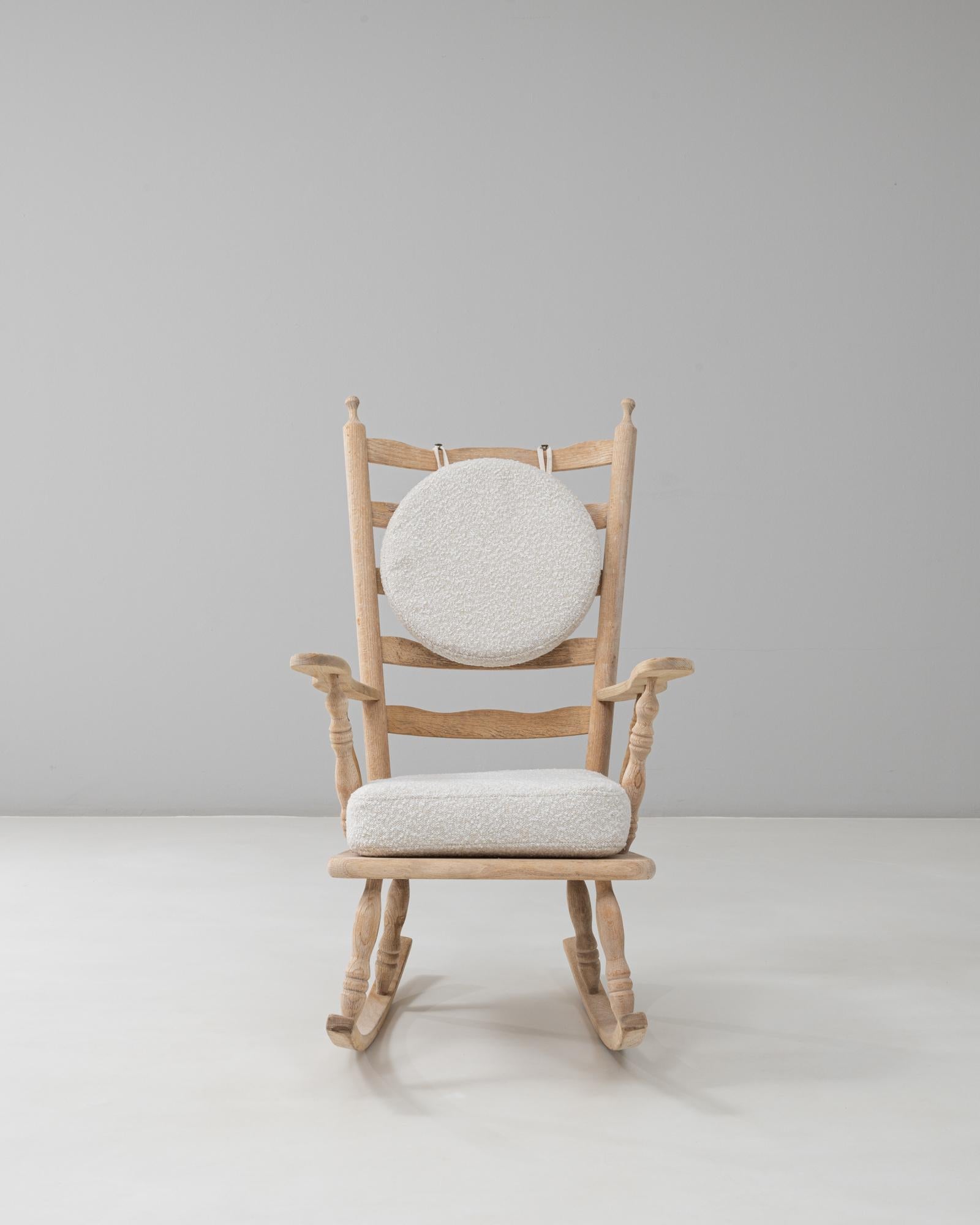 Ce rocking-chair en chêne français du 20e siècle offre un mélange charmant d'artisanat rustique et de confort contemporain. Le cadre, fabriqué en chêne légèrement patiné, présente des fuseaux tournés classiques le long du dossier et des accoudoirs,