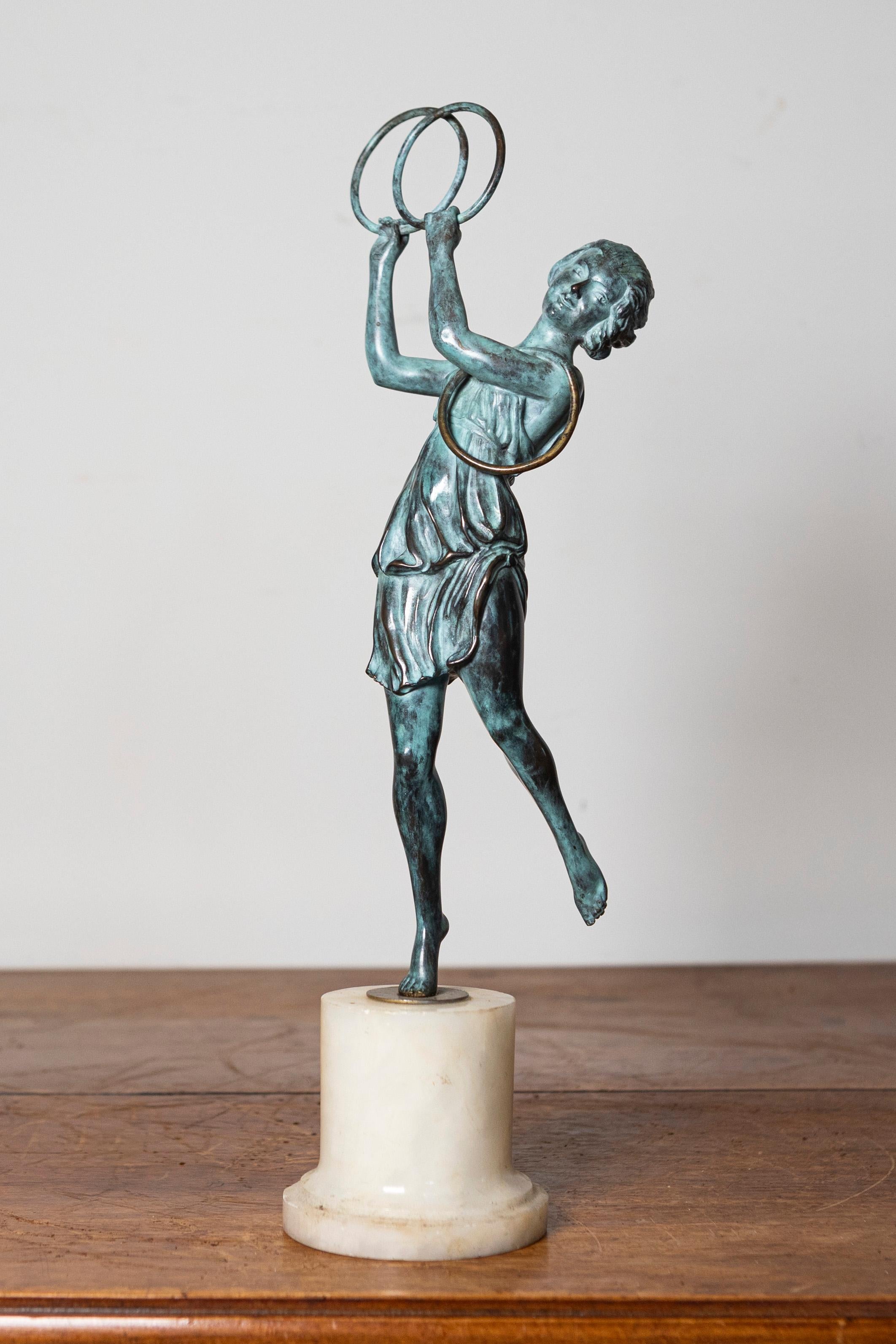 Questa elegante statuetta francese dei primi del Novecento cattura la grazia e il fascino di una figura femminile impegnata in un vivace momento di espressione artistica. Realizzata in bronzo patinato, la statuetta raffigura una giovane ballerina