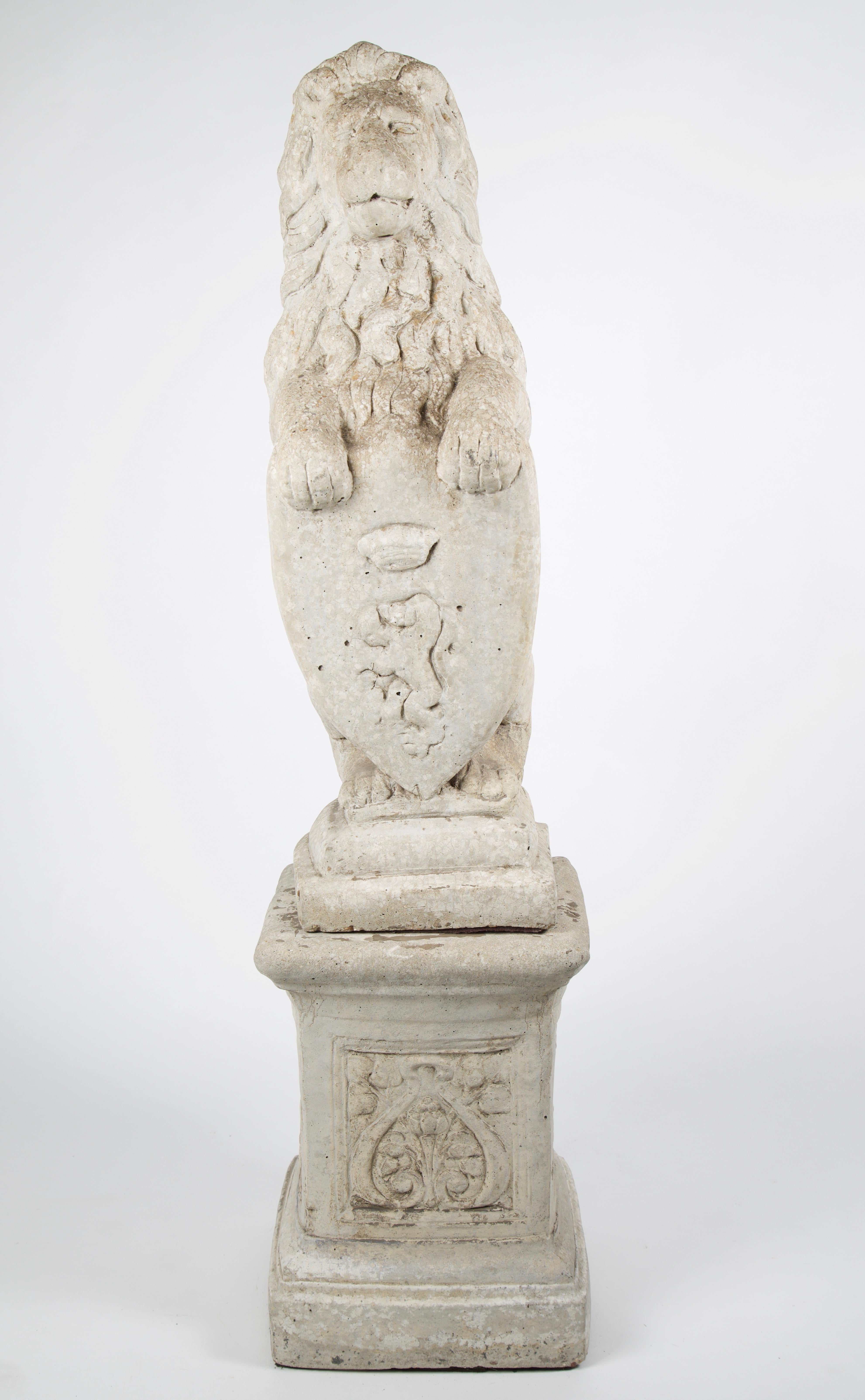 20th century French stone lion holding a shield on a pedestal. A 20th century lion carved from stone holding a crest carved with a lion with wearing a crown. It is a representation of power having exquisite detail while sitting atop a plinth base