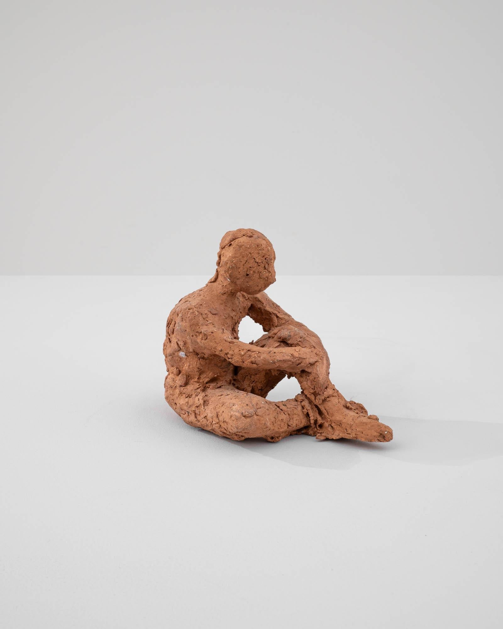 Cette sculpture contemplative en terre cuite française du XXe siècle invite à une pause de réflexion, capturant une figure solitaire dans un moment d'introspection. La texture rugueuse et non raffinée de la terre cuite confère à la pièce une