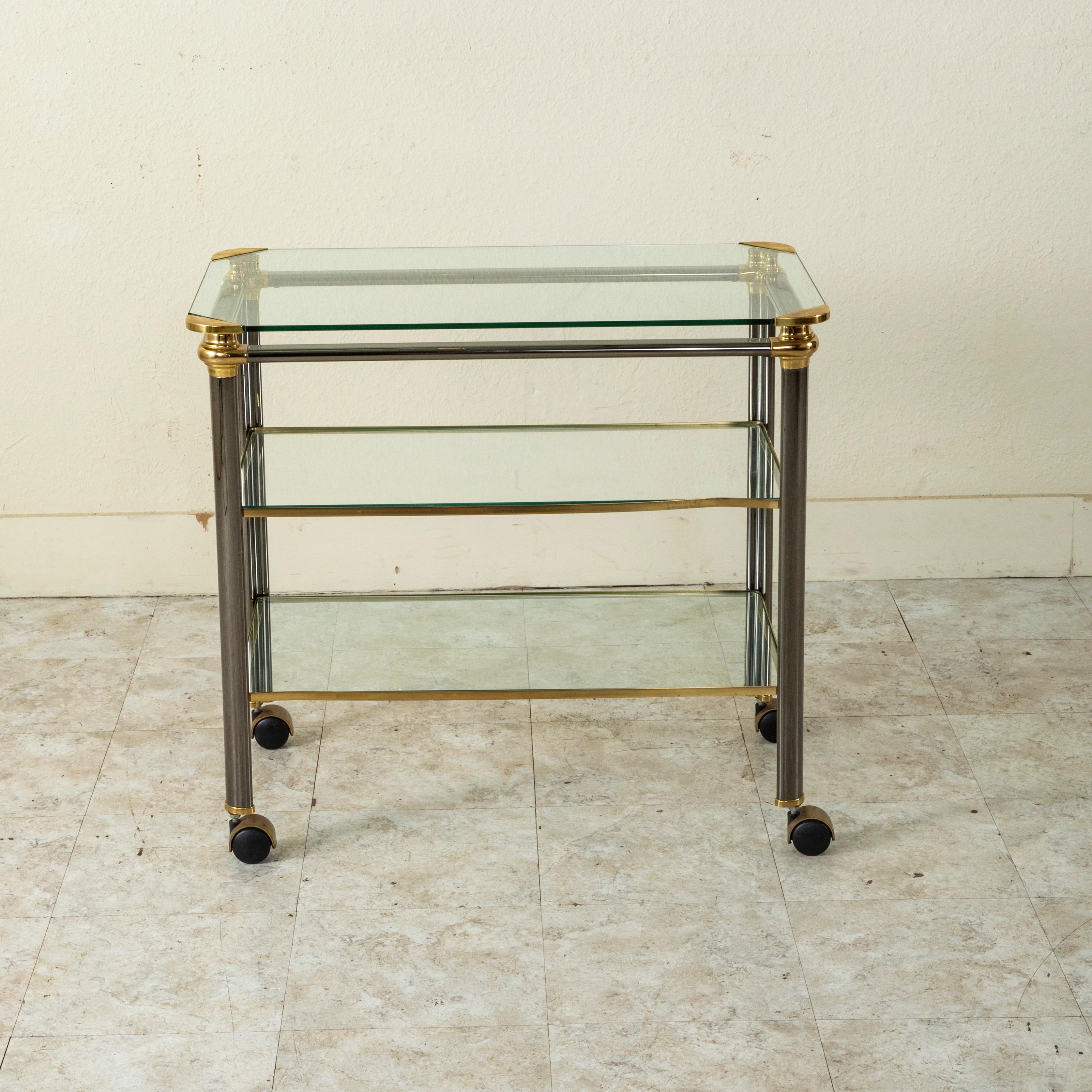 This mid-twentieth century French bar cart or trolley is designed with chrome legs and brass detailing. The bar cart rests on casters allowing for easy mobility. With three glass tiers, this piece provides layered display space for bar accessories