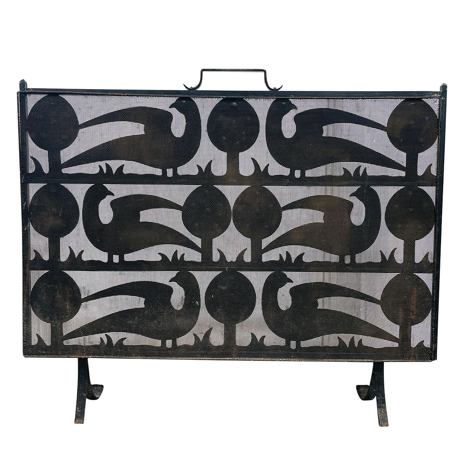A vintage Mid-Century modern French hand forged wrought iron fireplace screen of heavy gage, in good condition. The wrought iron raised screen depicts in geometrical manner six large peacocks and stylized trees. Topped with a central handle. Perfect