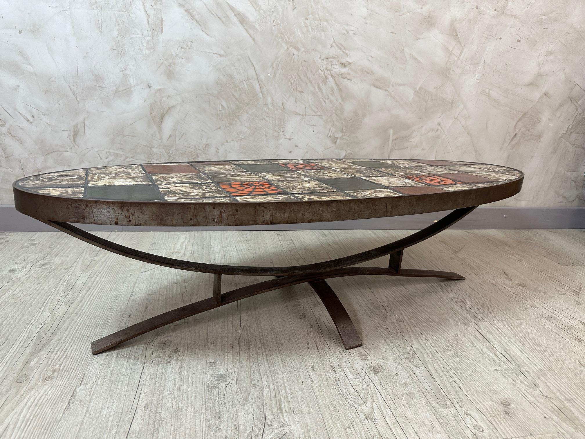 Magnifique table basse ovale des années 1960, dotée d'un remarquable plateau en carreaux de céramique dans des tons terreux de brun, de vert, d'ocre et d'orange vif, rappelant le travail artistique de Roger Capron.
La base en métal à pieds croisés,