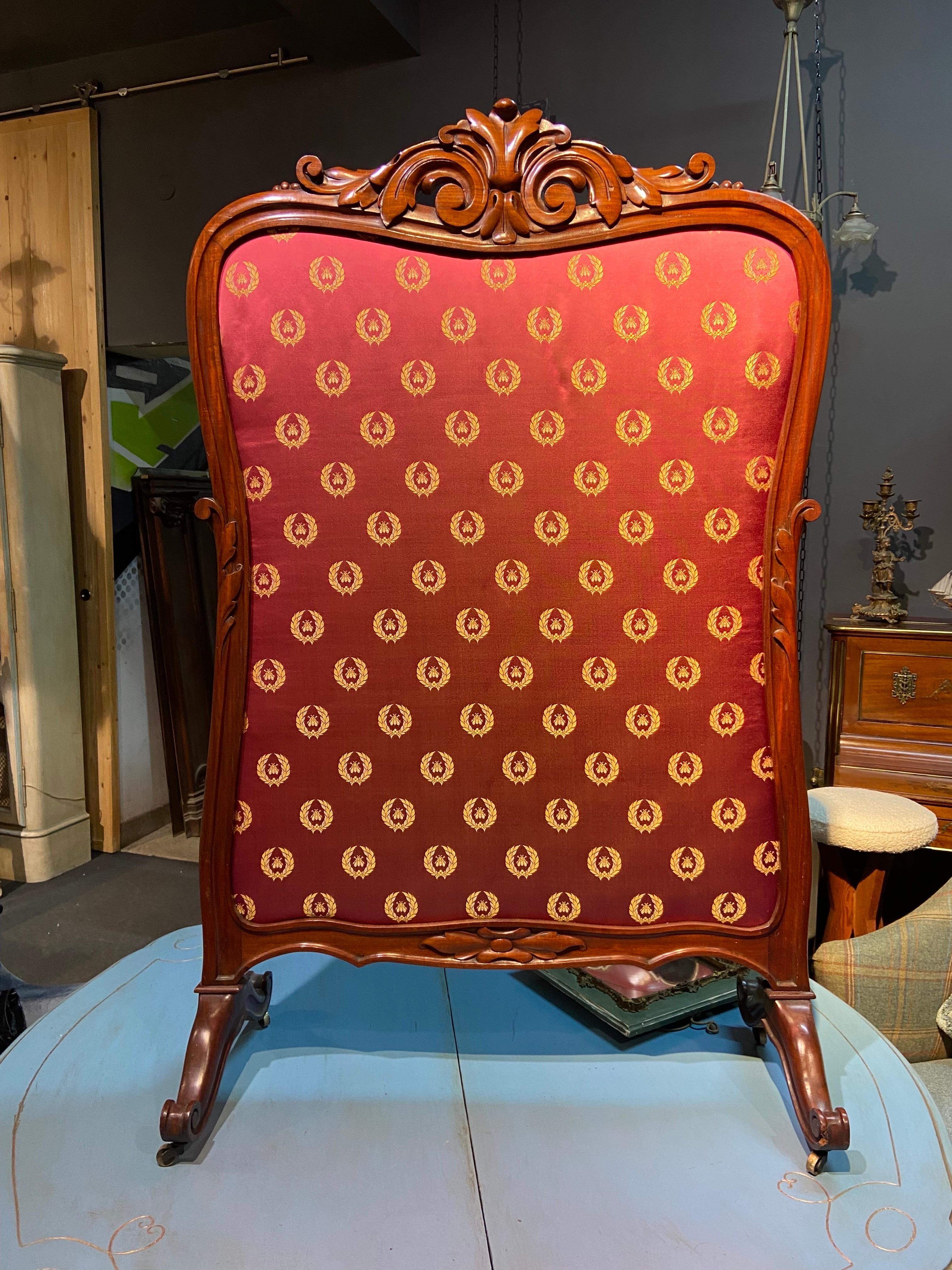 20th Century large hand carved wooden fire-screen upholstered in red silk fabric in front and light beige silk at the back. The frame has a centre decoration on the top and the carved legs are resting on small brass castors. Made in France in early