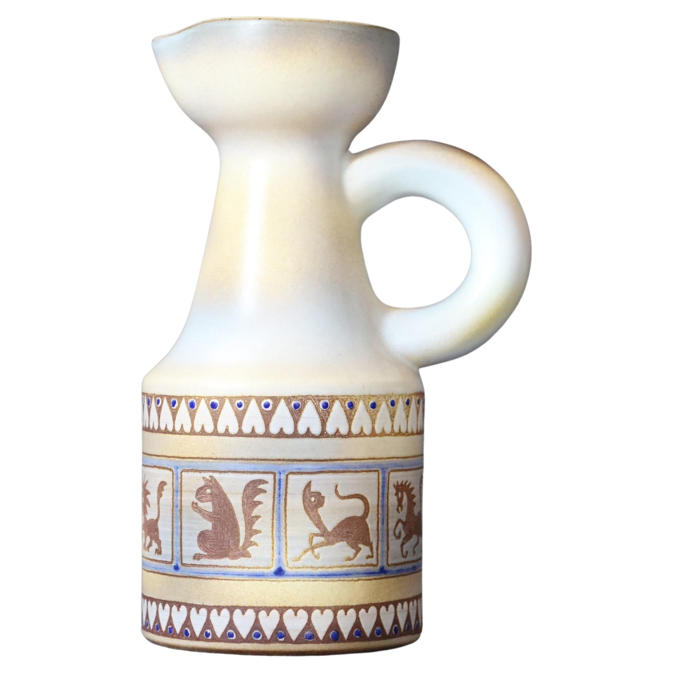 20th century French white ceramic pitcher by René Maurel, 1970's

The pitcher is glazed in a brilliant creamy white. It is decorated with an animal frieze with geometric motifs and colored in pale tones. 
It is signed. 
It is in a very good