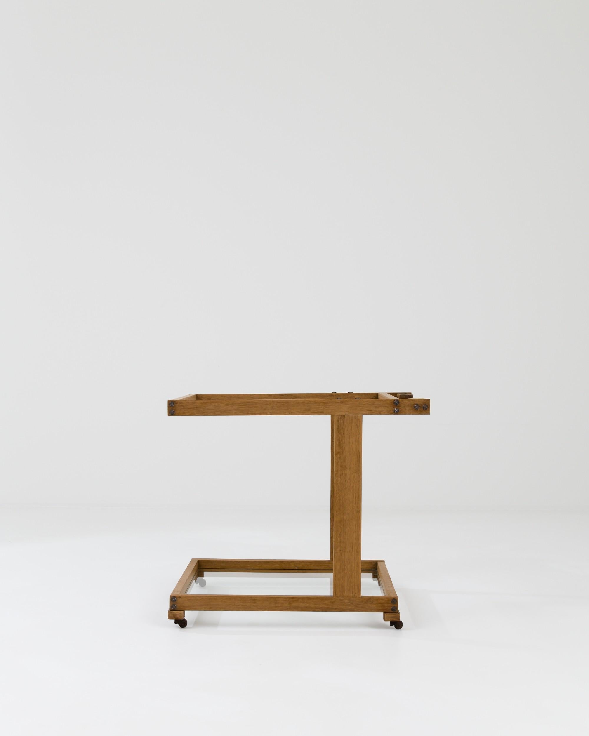 A wooden bar cart created in 20th century France. Minimal and stylish, yet also warm and rustic, this bar cart offers a truly unique look. Flawless mortise and tenon joinery and vintage hardware frame an upper and lower glass shelf, creating a