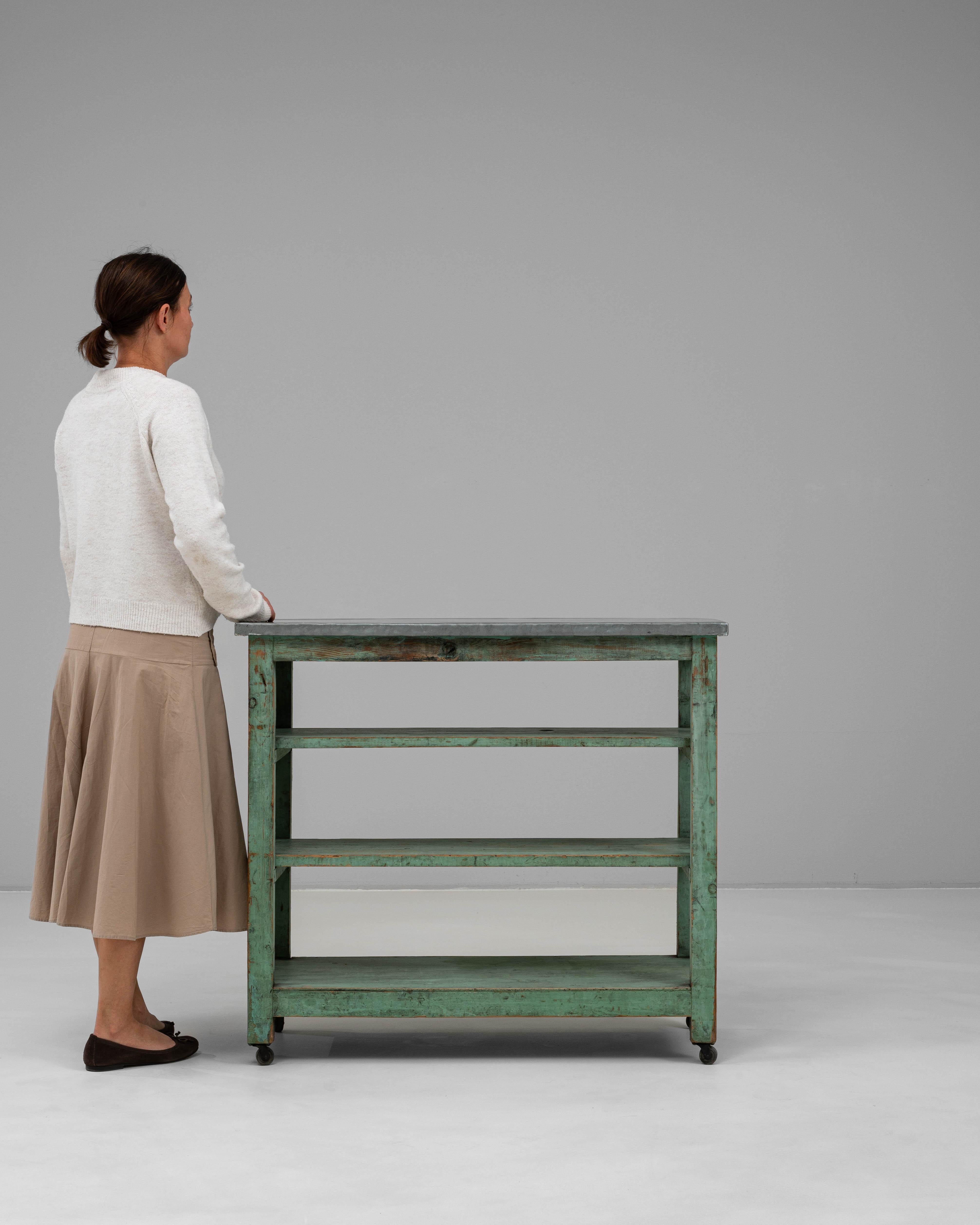 This 20th century French wooden bar cart blends industrial utility with vintage charm. Featuring a distressed green-painted frame and a weathered zinc top, the piece offers both durability and character. Three open shelves provide ample storage for