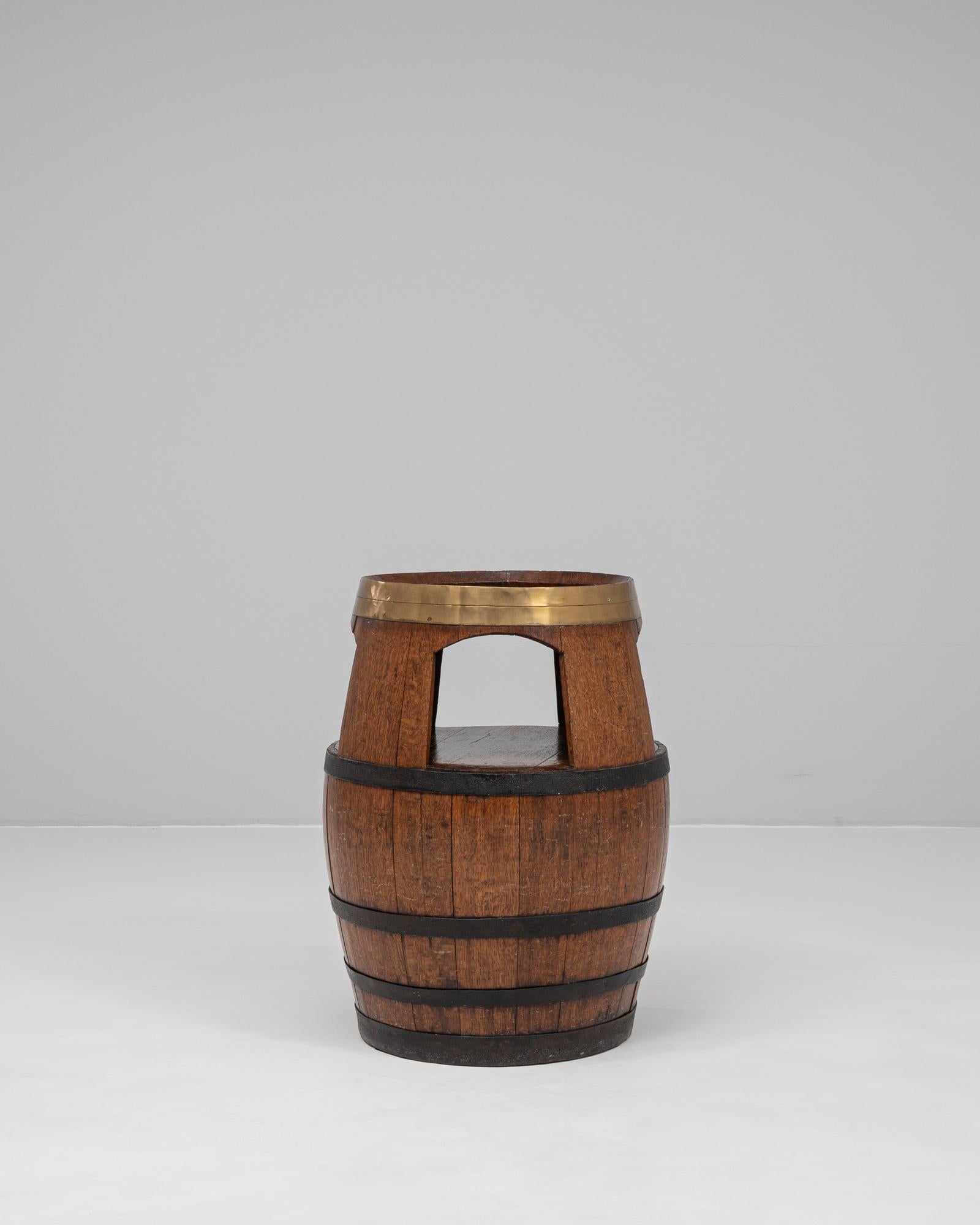 This 20th Century French wooden barrel table offers a charming blend of rustic utility and vintage character. Crafted from solid oak staves bound by iron bands, the barrel retains its authentic silhouette while incorporating a functional open shelf