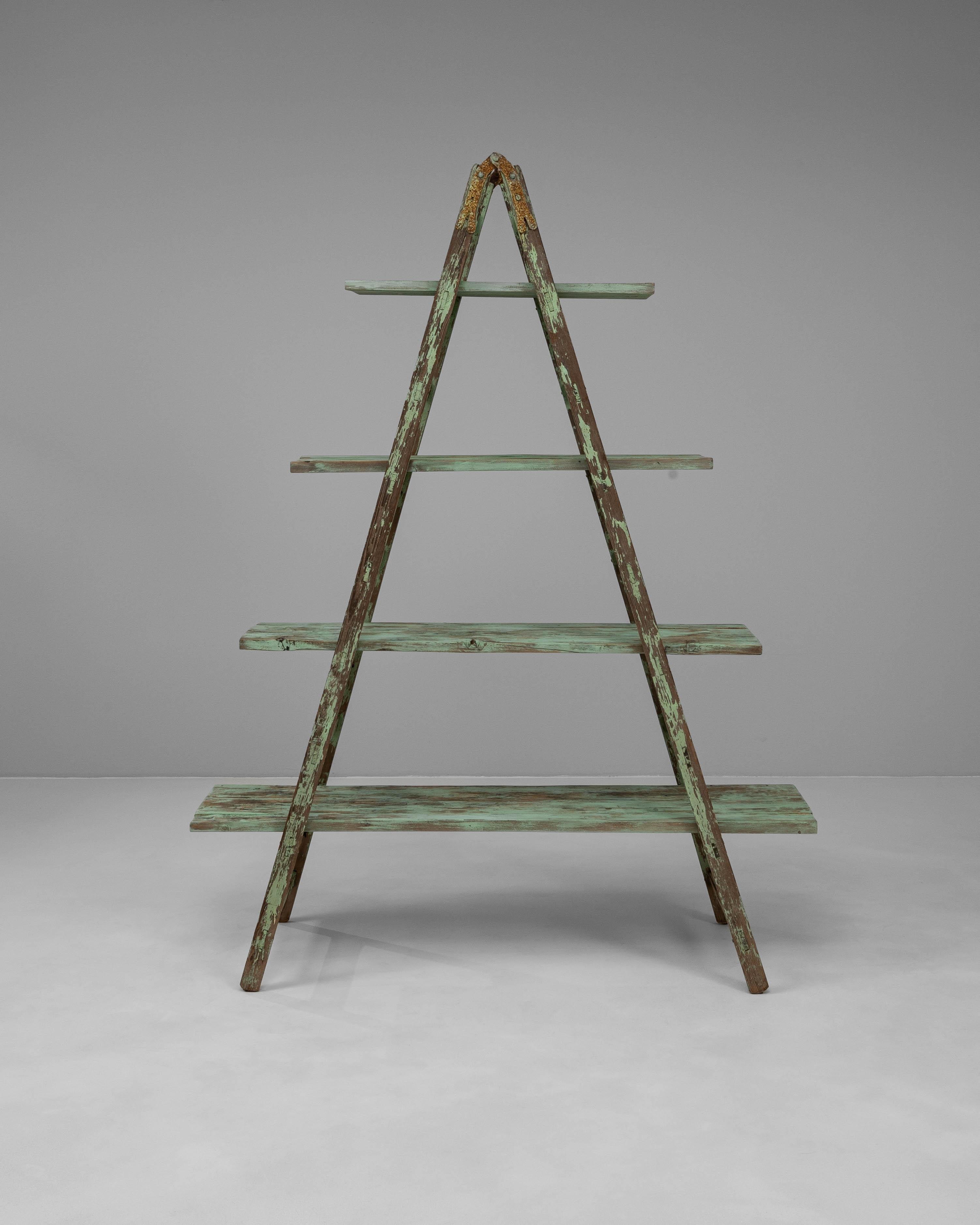 This 20th Century French wooden bookcase offers a sculptural, utilitarian charm with its unique A-frame ladder form and distressed green patina. Originally used as a functional ladder, it has been thoughtfully converted into a tiered shelving unit,