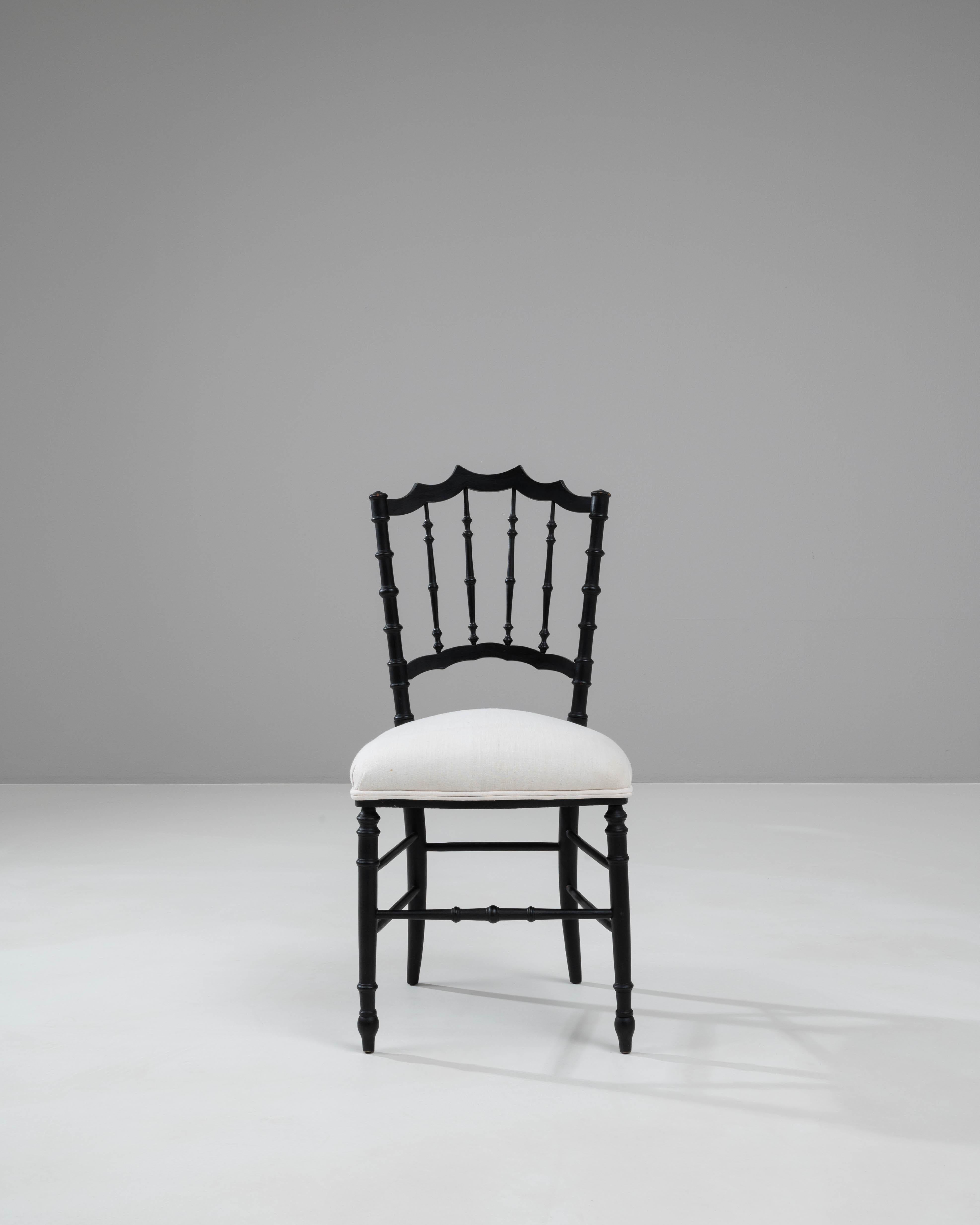 Dieser französische Holzstuhl aus dem 20. Jahrhundert ist ein Musterbeispiel für klassische Eleganz und anspruchsvolles Design. Das Gestell ist in einem eleganten, matten Schwarz lackiert und weist wunderschön gearbeitete Spindeldetails und eine