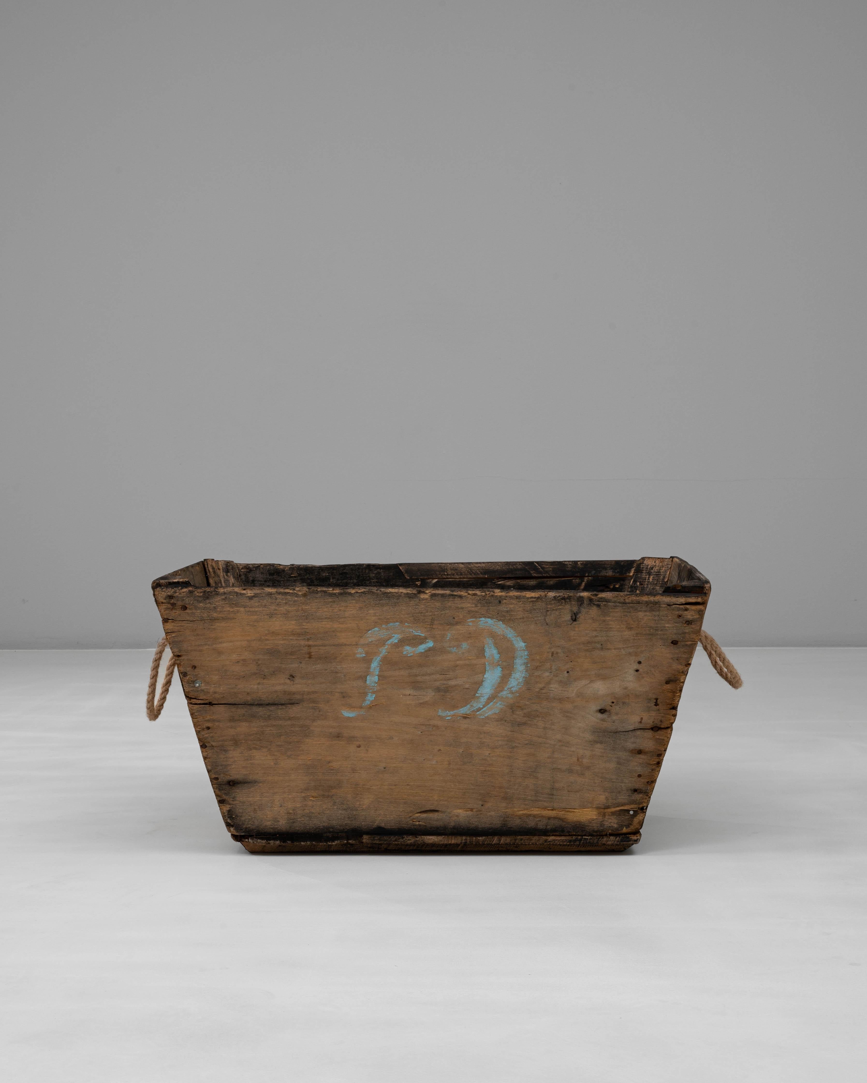 Esta cesta de madera francesa del siglo XX para vendimiar champán encarna el encanto utilitario de las tradiciones vitivinícolas rurales. Fabricada en madera maciza con asas de cuerda, se utilizaba originalmente en la región de Champaña para recoger