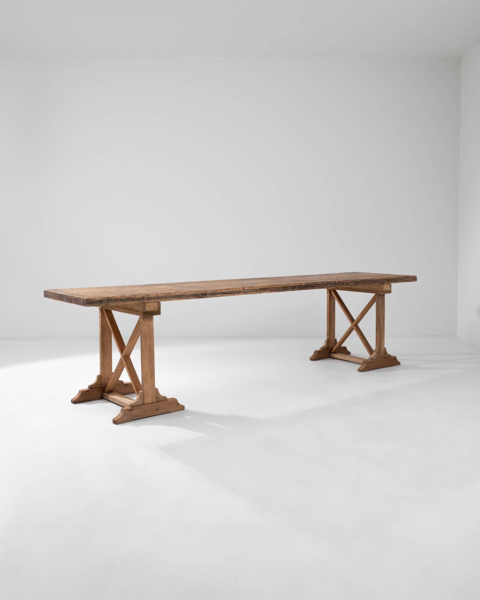 This vintage wooden dining table makes a handsome country centerpiece. Made in France in the 20th century, the form has a rustic simplicity: a long rectangular tabletop sits atop trestle legs, braced with bold X-shaped struts. The clean corners of