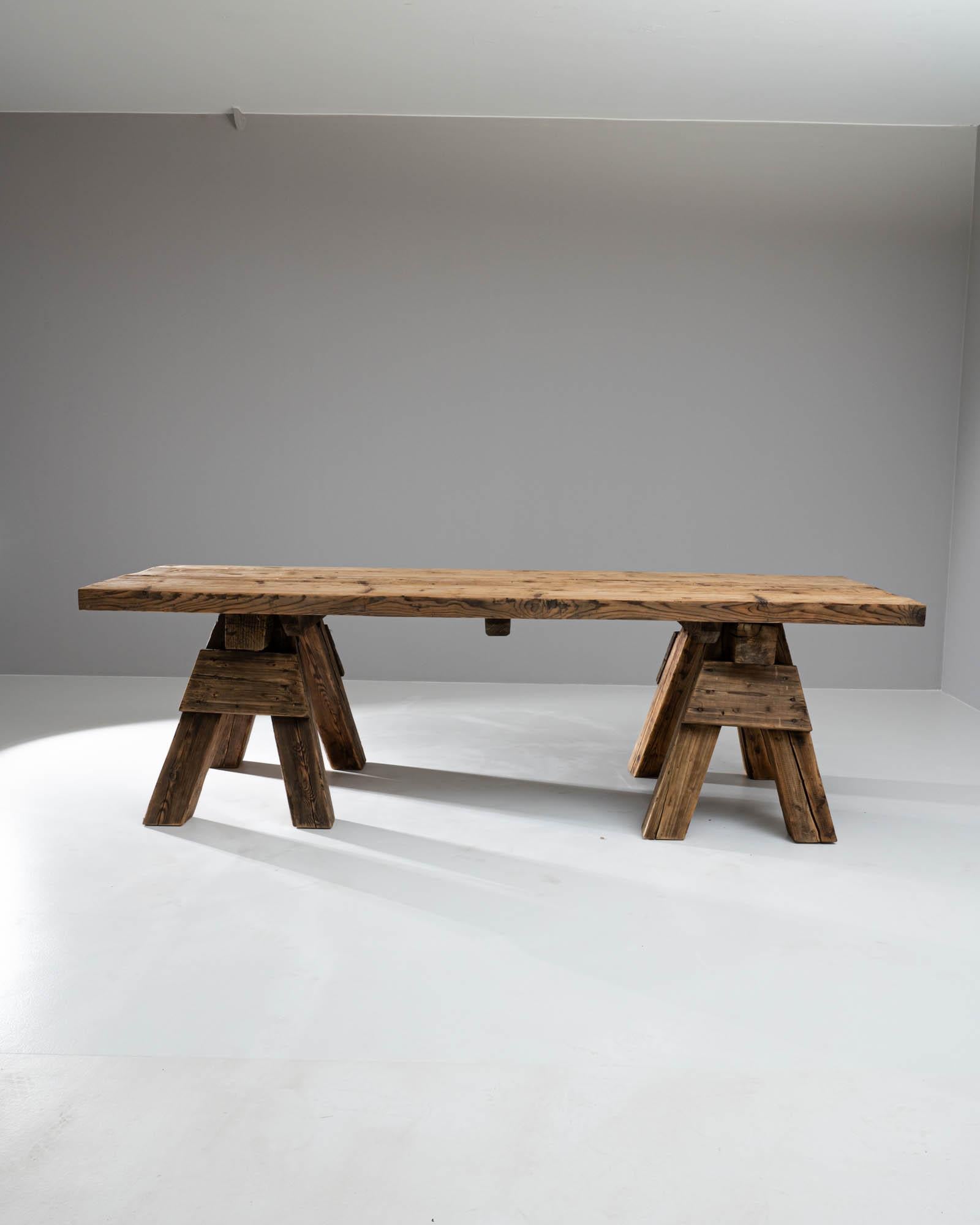 This magnificent 20th Century French wooden dining table exudes rustic elegance and robust charm, making it a perfect centerpiece for your dining area. Crafted from richly textured reclaimed wood, this table showcases natural imperfections and grain