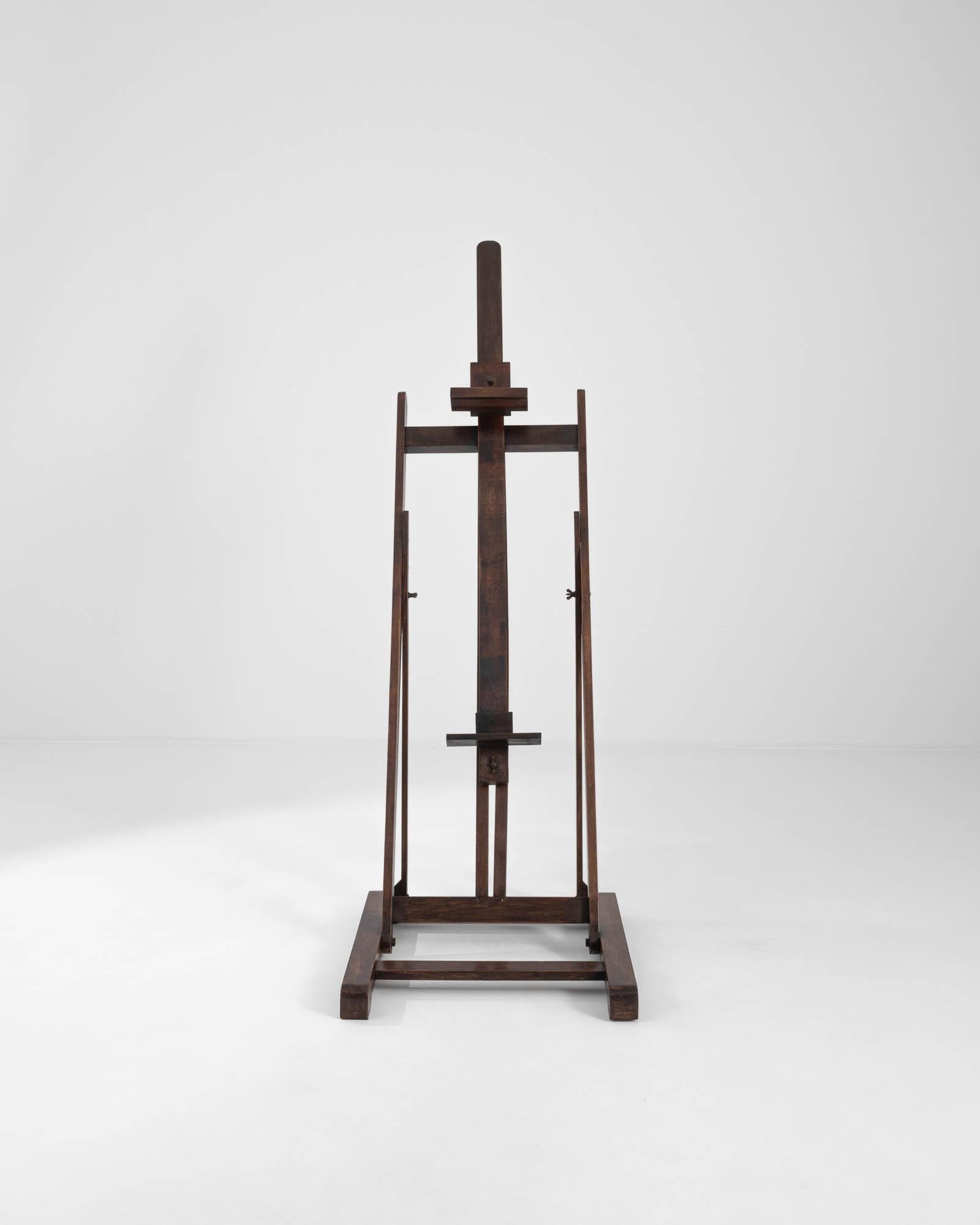 A 20th century wooden easel produced in France. Standing upright with a composed posture, this adjustable easel is ready for its next job. The richly stained wood creates an approachable palette, inviting its next artist to inspire their creativity.