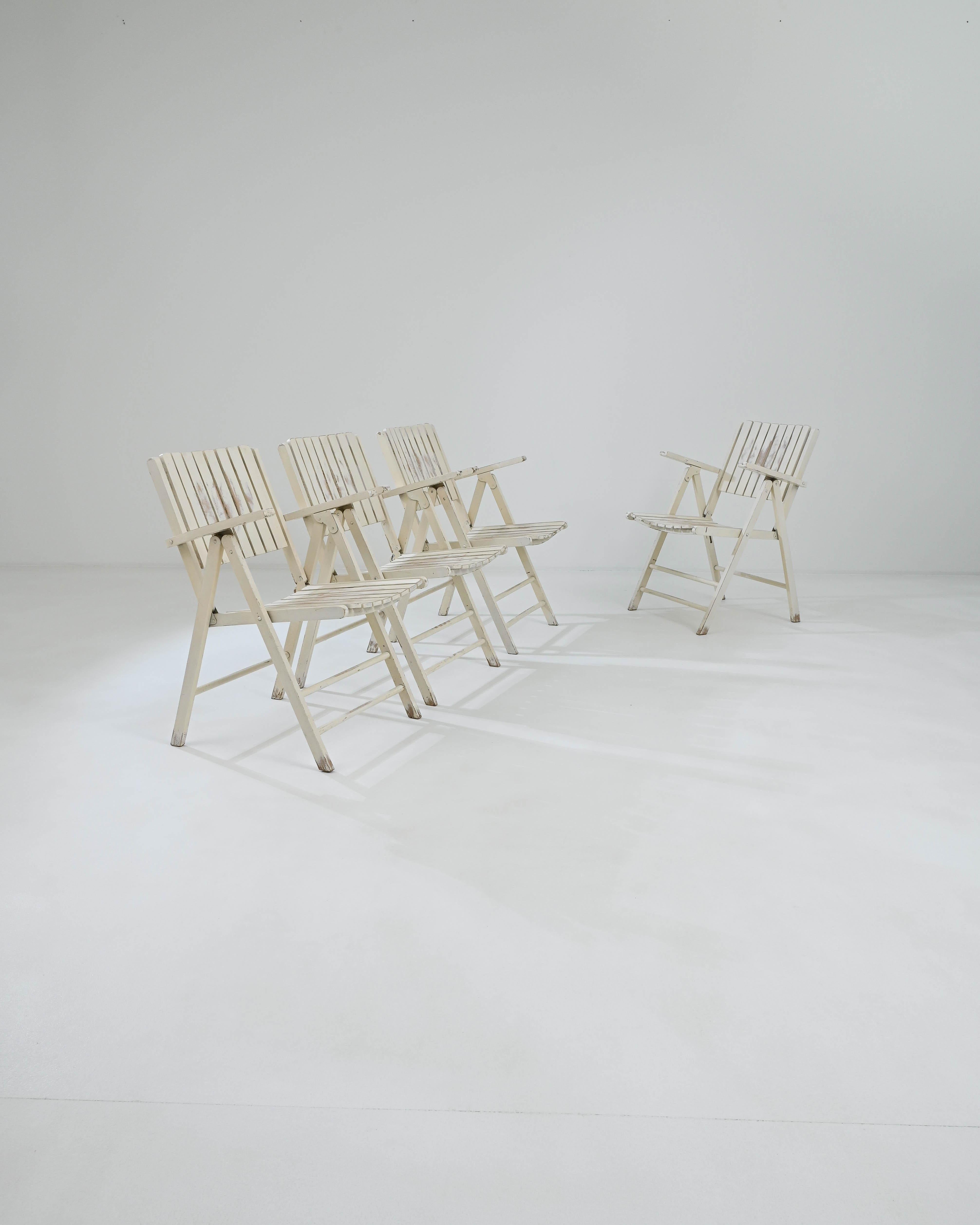 A set of wooden folding outdoor chairs created in 20th century France. Collapsible lawn chairs clad in a pleasing off-white tone, these antique chairs communicate a lovely matured cheer. Composed of wooden slats which line the backs and seats, these