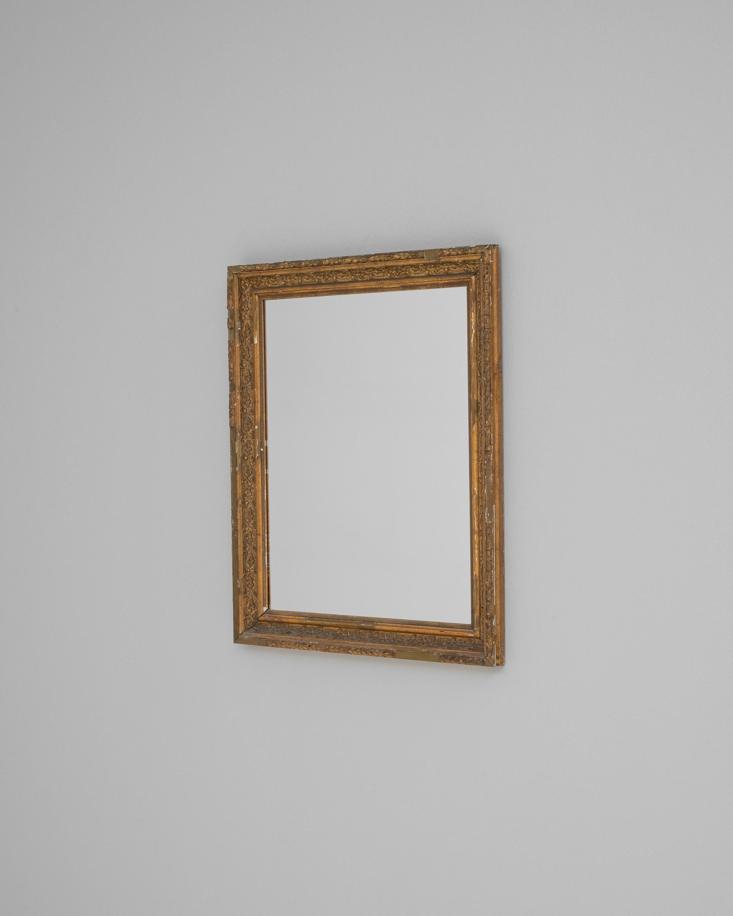 Discover the allure of vintage charm with this 20th Century French Wooden Mirror, a piece that beautifully marries function and form. The mirror is framed in meticulously carved wood, with a distressed gold finish that highlights the intricate