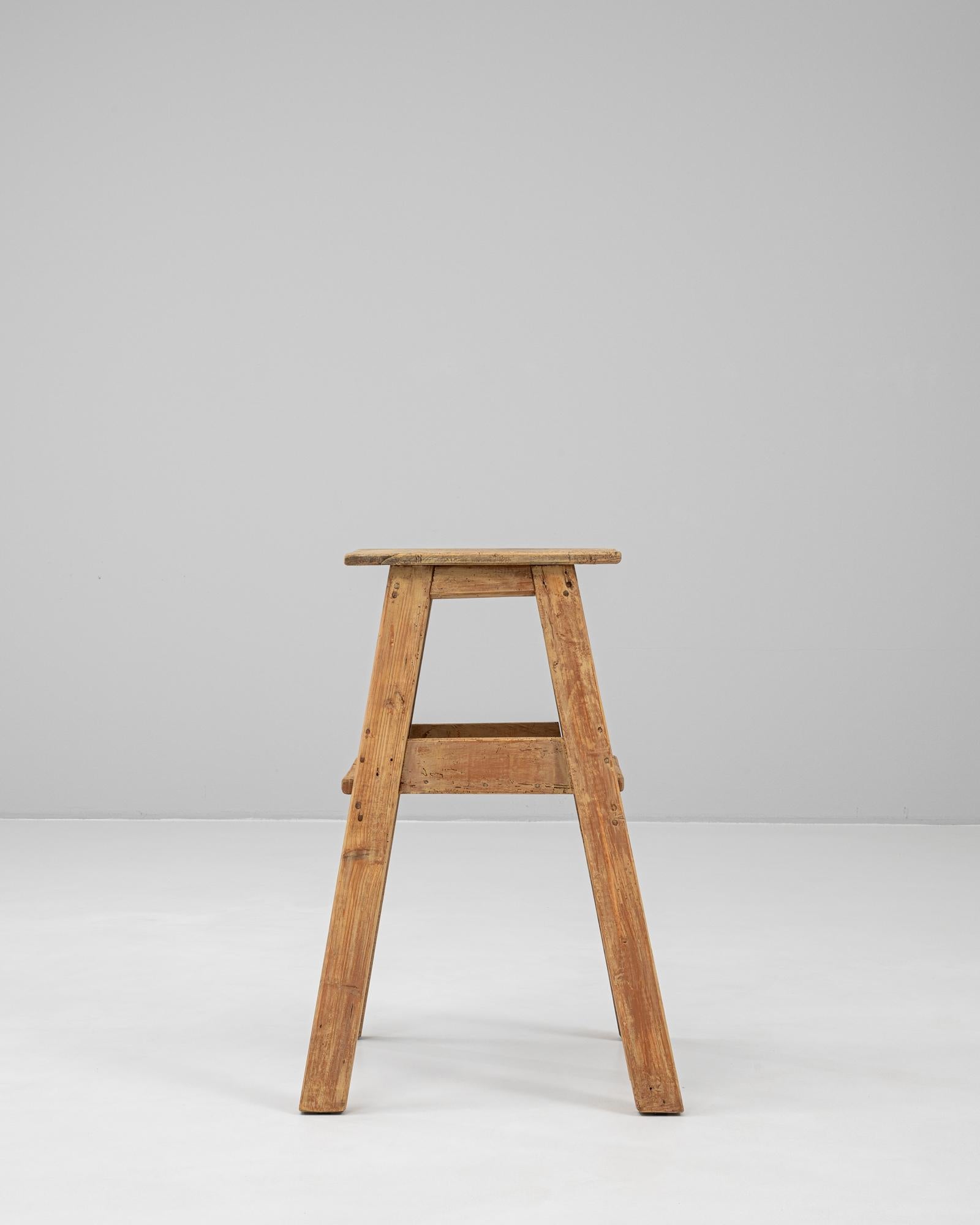 Este pedestal de madera francés del siglo XX encarna el encanto rústico con su robusta construcción artesanal. Fabricada en madera maciza con una hermosa pátina envejecida, presenta un diseño sencillo pero funcional, con cuatro patas separadas y
