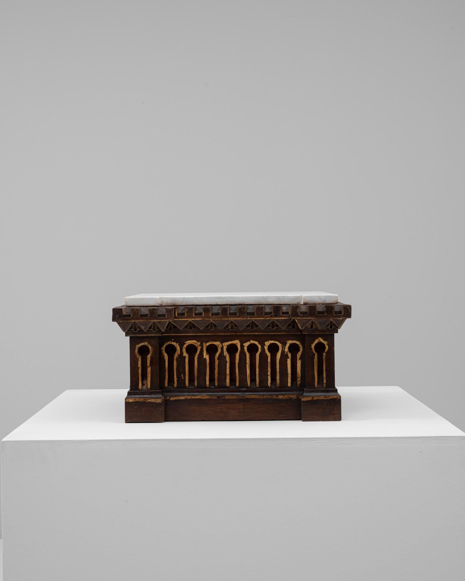 Questo piedistallo in legno francese del XX secolo con piano in marmo unisce dettagli architettonici a una pratica presenza scultorea. La base è realizzata in legno tinto di scuro e presenta intricati motivi intagliati che ricordano il design del