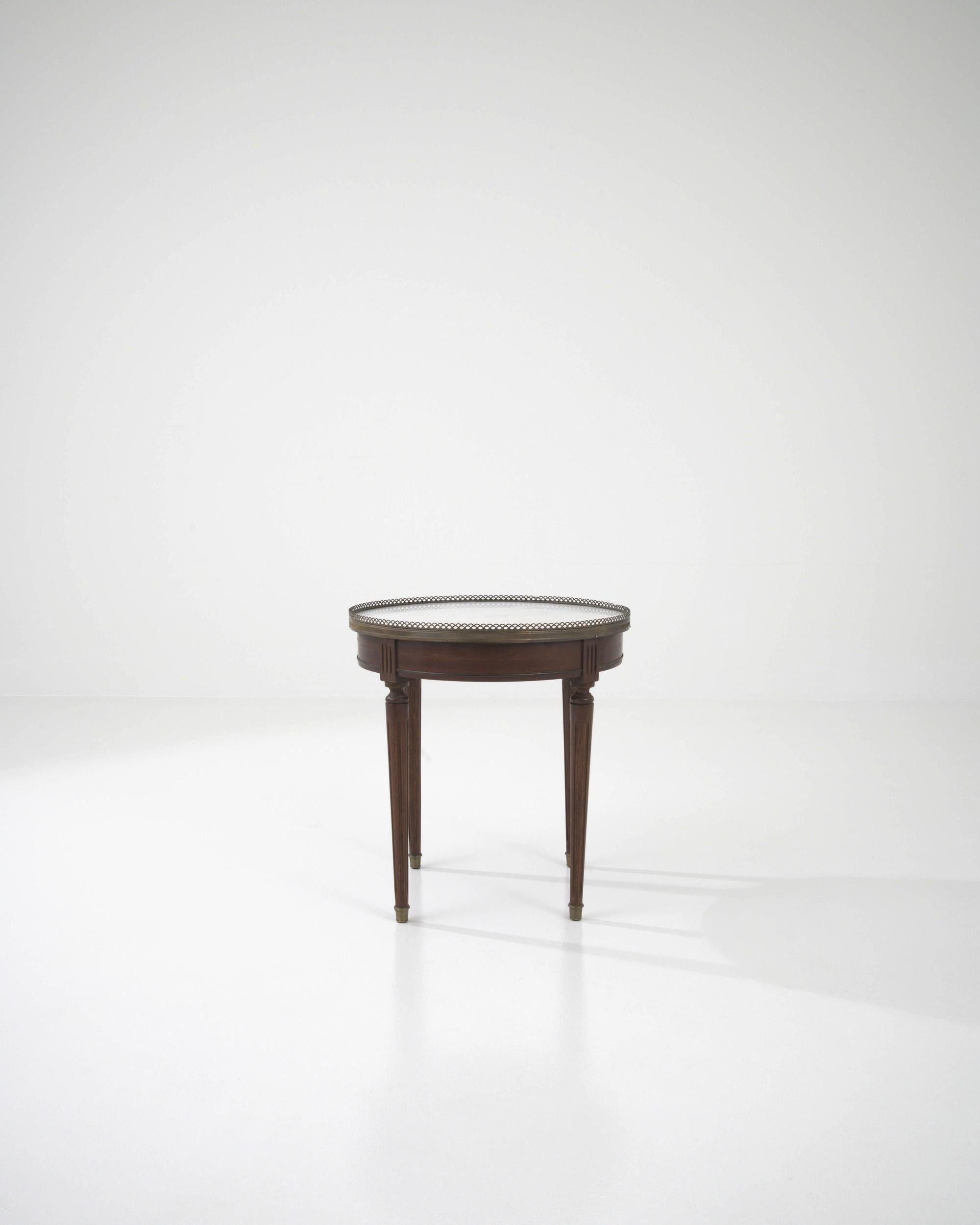 Crafted in France at the beginning of the 20th century, this petite side table flaunts a round white marble top framed in skillfully formed brass edging. A few carved elements adorning the base, made of rich dark wood, reveal a high level of taste