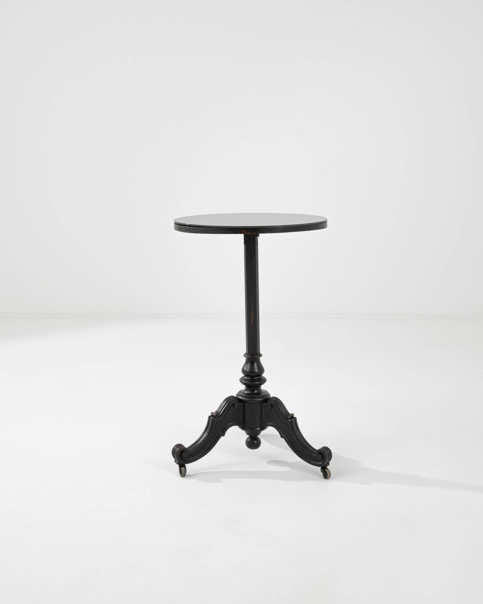This vintage wooden side table on wheels offers a sophisticated period piece. Made in France in the 20th century, a circular tabletop sits atop a faceted central column; the cascading scrolls of the tripod feet create an elegant profile. Small