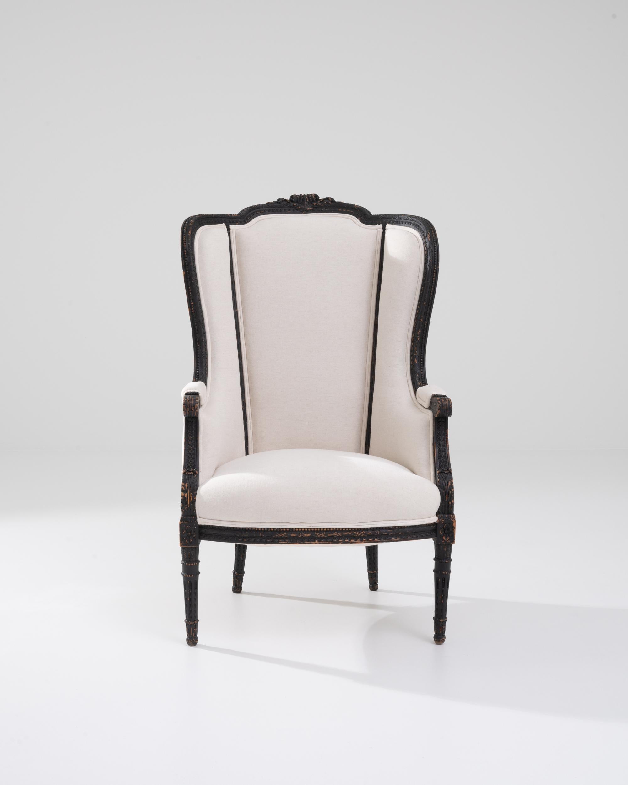 A wooden upholstered armchair created in 20th Century France. This high-backed armchair oozes both an old-world elegance as well as a warm and approachable demeanor. The fresh off-white fabric that dawns its cushioning stands in pleasing contrast to