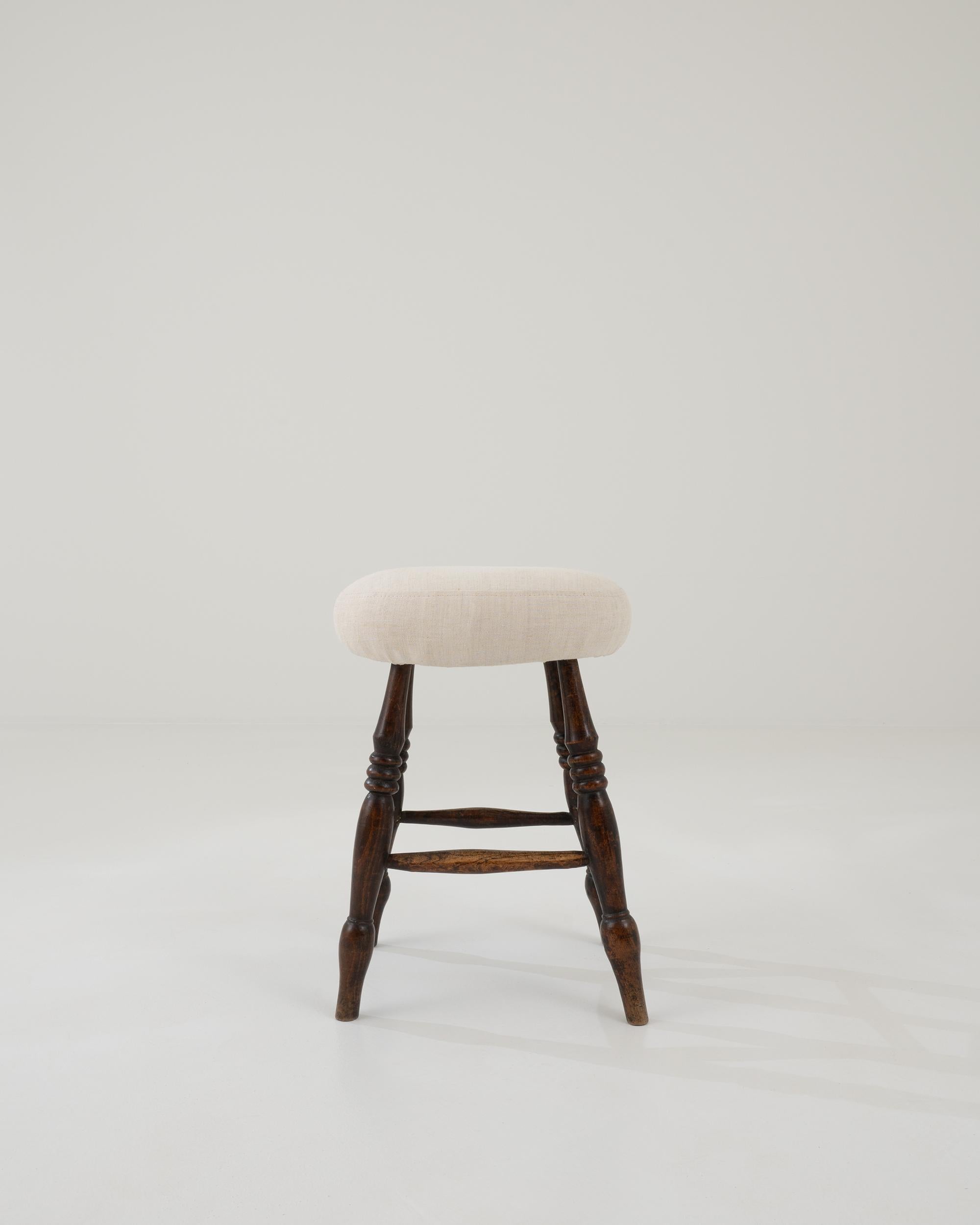 A wooden stool with an upholstered seat created in 20th century France. Rustic and full of warmth, this small and modest stool quietly imparts its age and experience. A gentle patina has formed along the lathed stretchers, indicating a place where