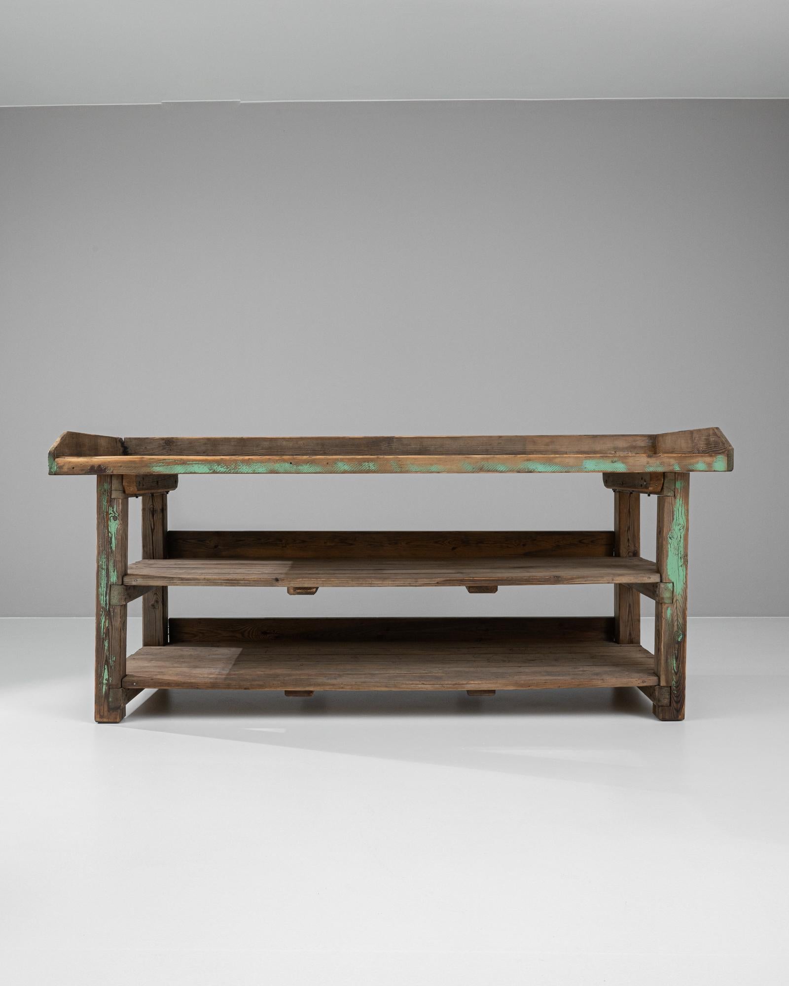 This 20th-century French wooden work table encapsulates the rustic charm and utilitarian spirit of its time. Featuring sturdy construction, the table boasts a robust wooden top and frame accented with remnants of original teal paint, adding a touch