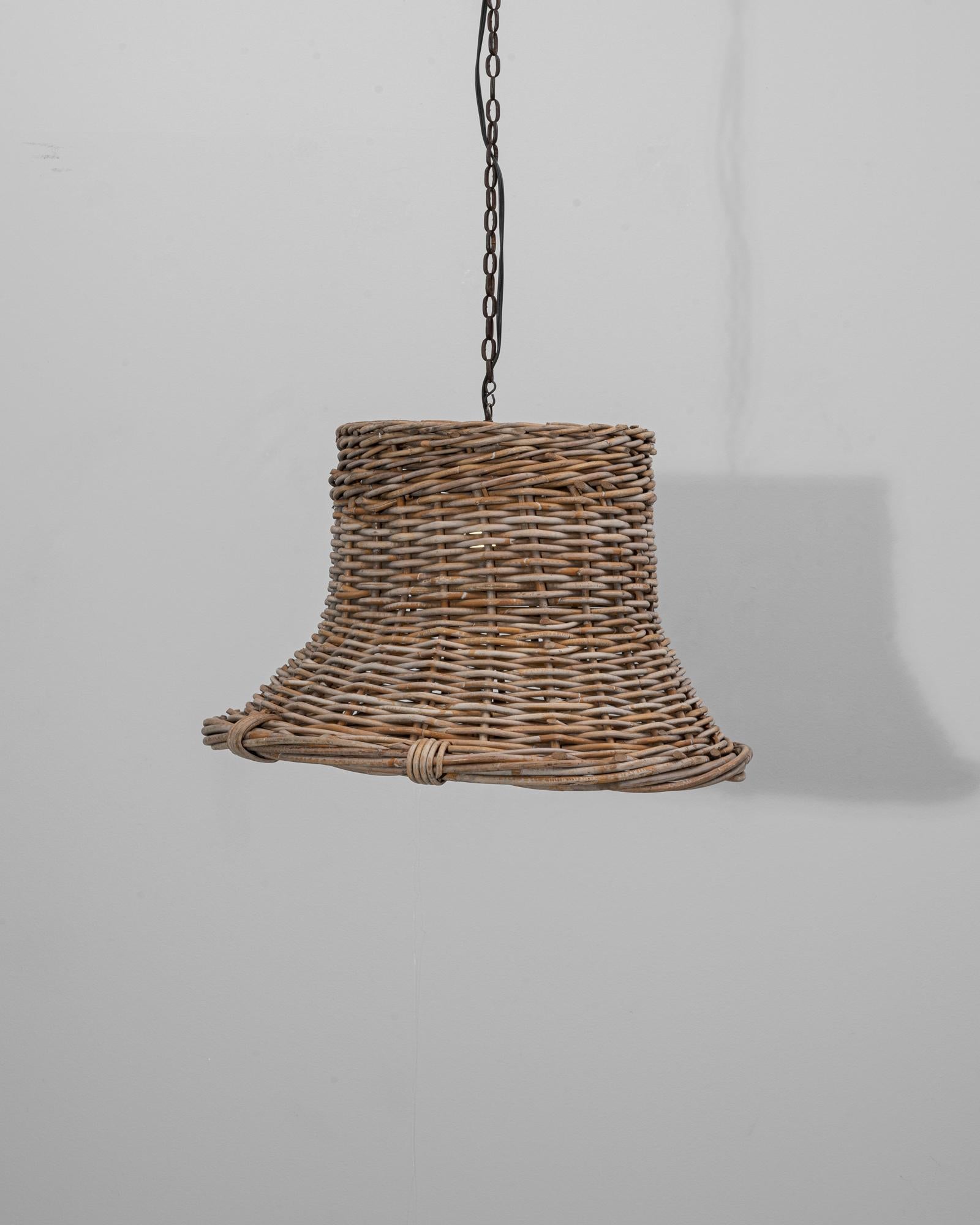 Diese französische Pendelleuchte aus dem 20. Jahrhundert hat einen handgeflochtenen Rattanschirm in anmutiger Glockenform, der rustikalen Charme und handwerkliches Können ausstrahlt. Die natürliche Textur und die organische Krümmung des Rattans