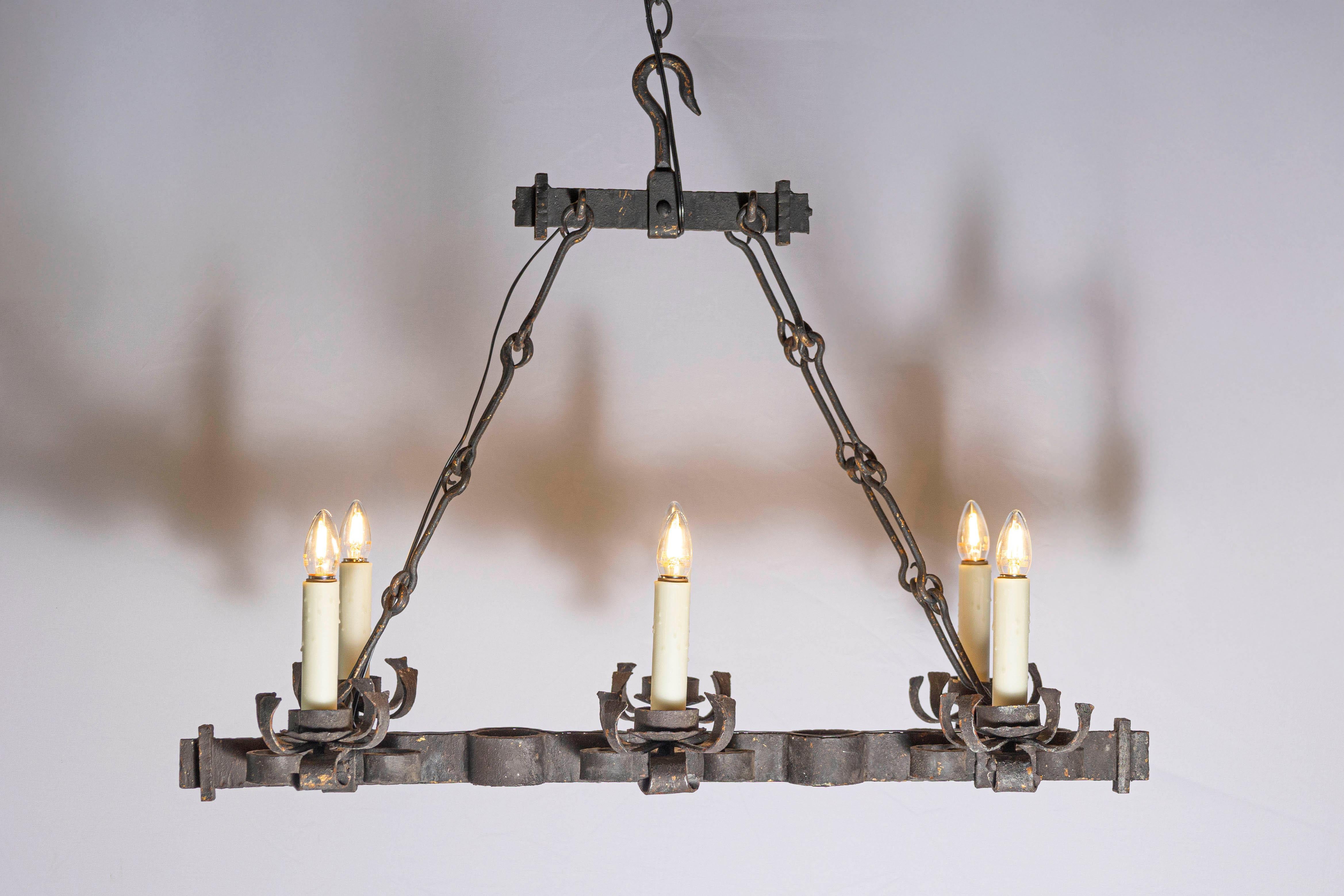 Questo lampadario in ferro battuto francese del XX secolo è un esempio di eleganza rustica grazie alla sua struttura robusta e al suo design artigianale. Caratterizzato da una struttura lineare sospesa da pesanti catene di ferro, questo lampadario