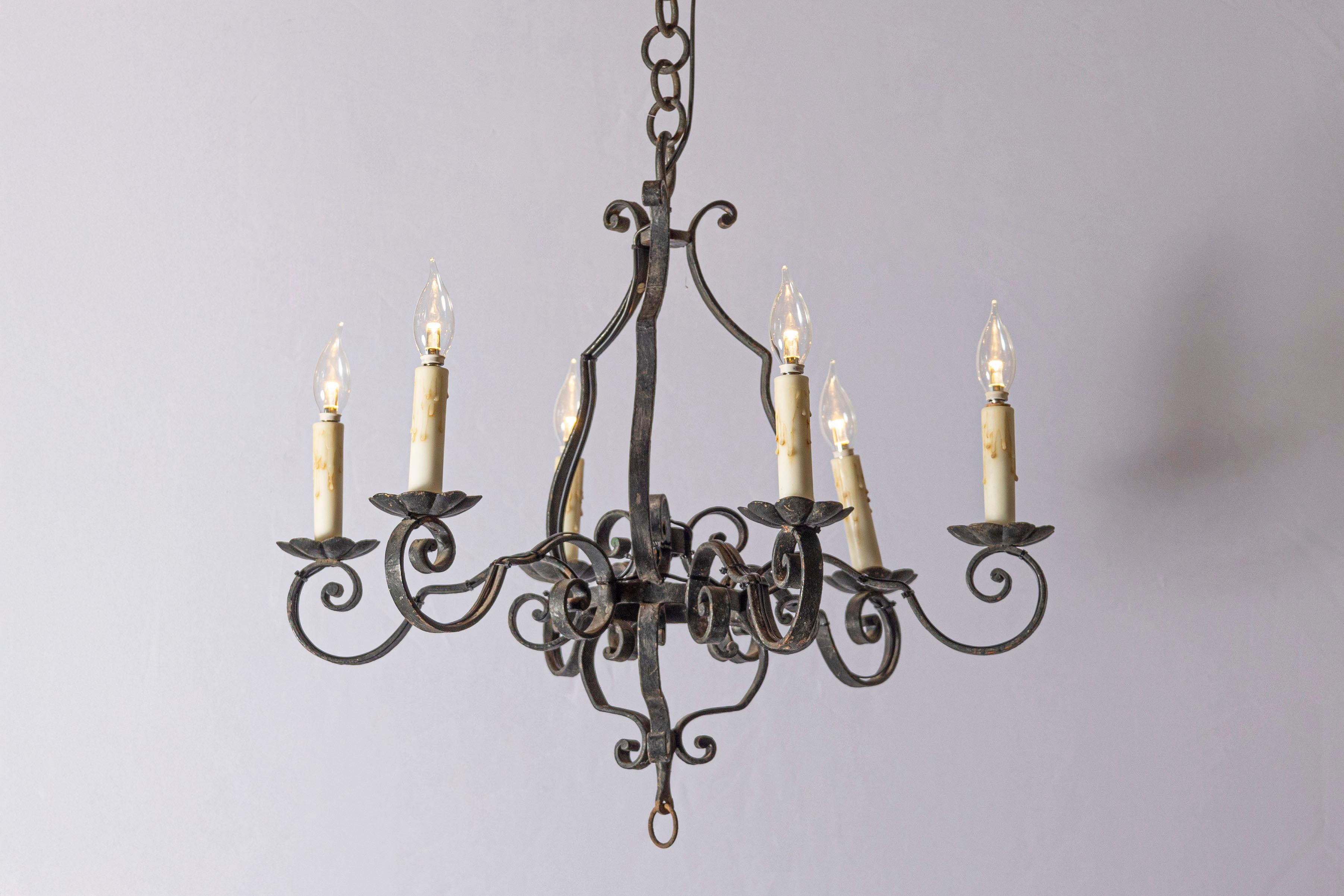 Si tratta di una coppia di lampadari in ferro battuto francesi del XX secolo, che mostrano un'elegante maestria con le loro intricate volute e le luci a candela. Ogni lampadario è progettato con sei bracci che conferiscono un aspetto simmetrico ed