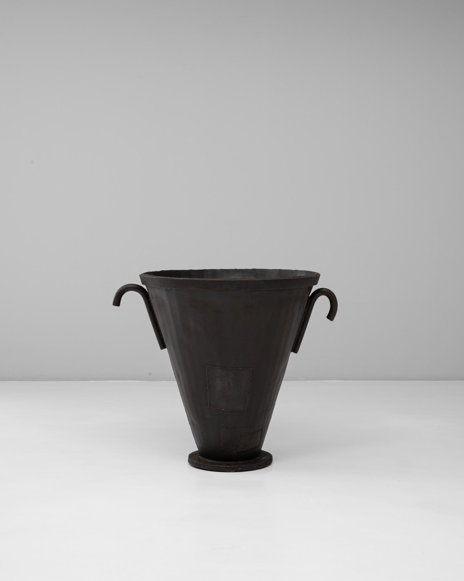 Cette cheminée à urne évasée en fer forgé français du 20e siècle incarne la force industrielle avec une silhouette sculpturale. Fabriqué avec un corps conique effilé, il repose sur une base circulaire robuste et présente des poignées audacieuses et