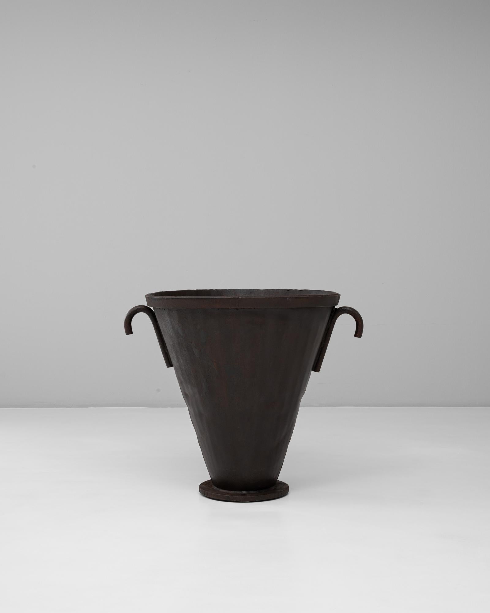 Questa urna svasata in ferro battuto francese del XX secolo esemplifica l'artigianato industriale rustico con la sua forma scultorea e audace. Realizzato in ferro pesante, il pezzo presenta una silhouette conica che si allarga con grazia verso il
