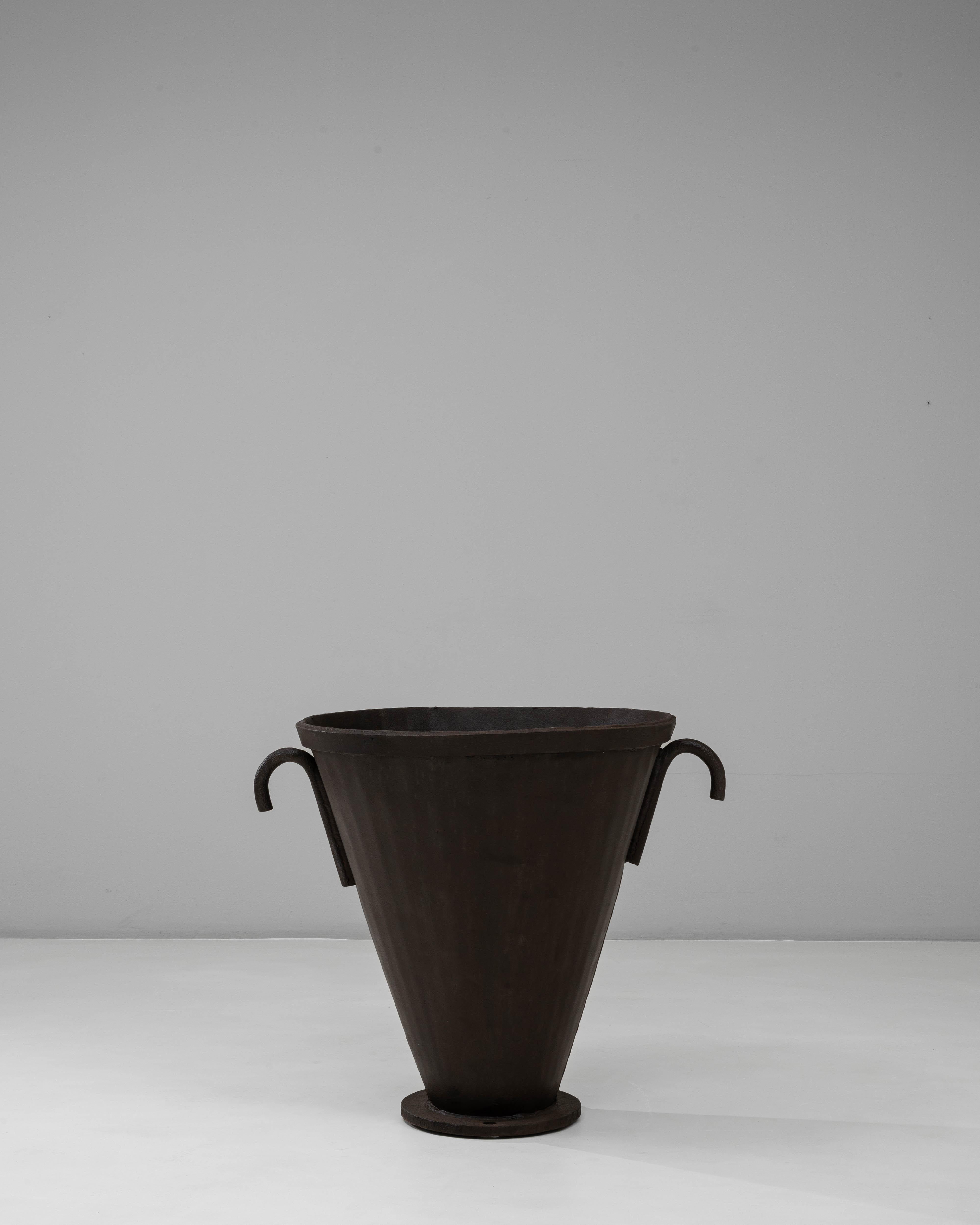 Un caminetto a urna svasata in ferro battuto del XX secolo, caratterizzato da una silhouette scultorea e da una presenza consistente. La forma conica si erge da una base circolare e si espande in un ampio bordo, creando un profilo audace e