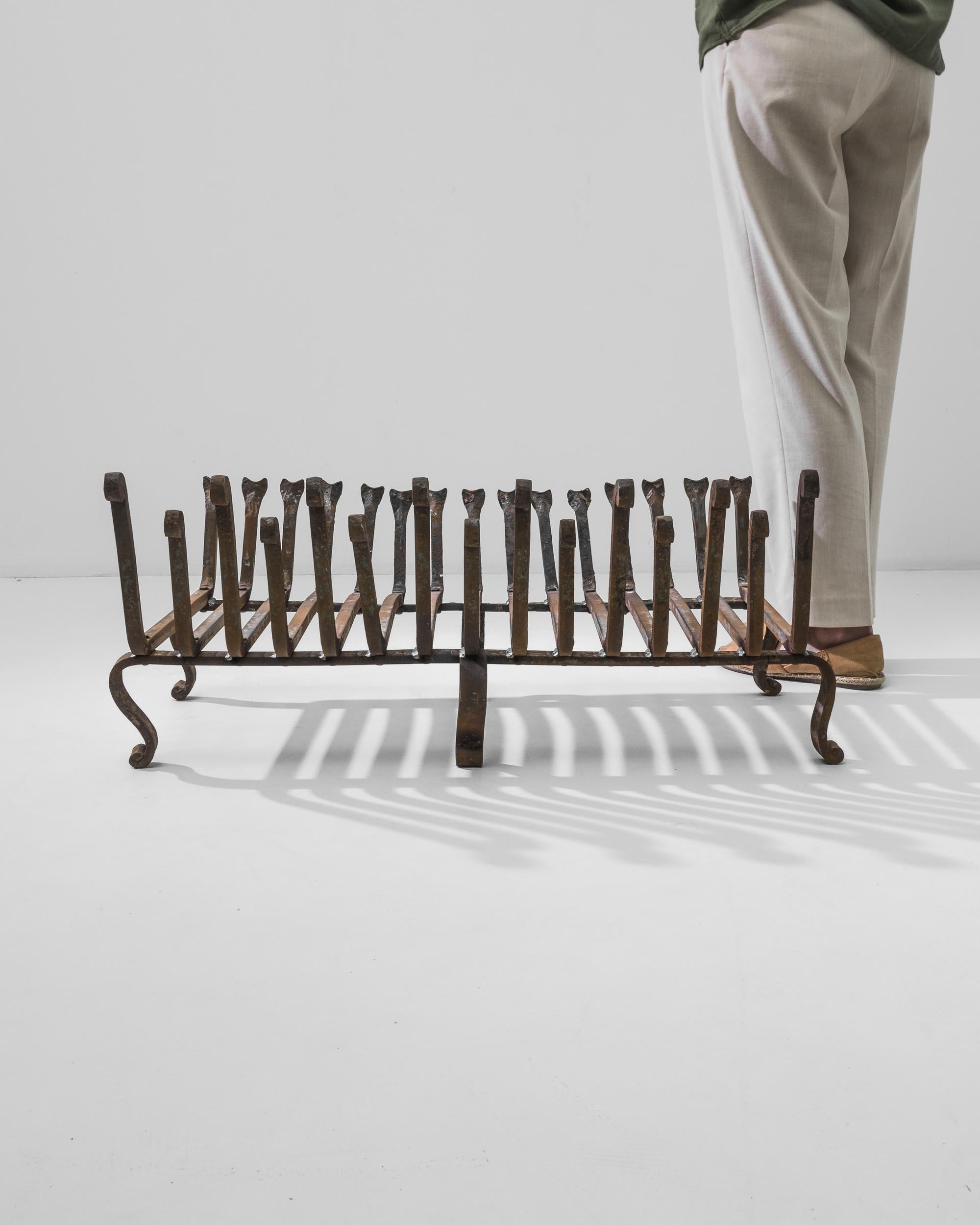 This French iron grate makes a unique centerpiece, evoking the ancient practice of fire-building and the elemental comforts of the hearth. Though made in the 20th Century, the age-old techniques used to craft cast iron give this piece a timeless