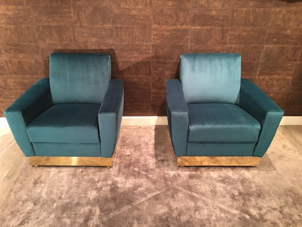 Pair of Italian  armchairs with a rectangular shape. They are very comfortable and enveloping. They are covered in turquoise velvet. The structure rests on a solid wooden base covered in polished brass. To facilitate movement, there are four little