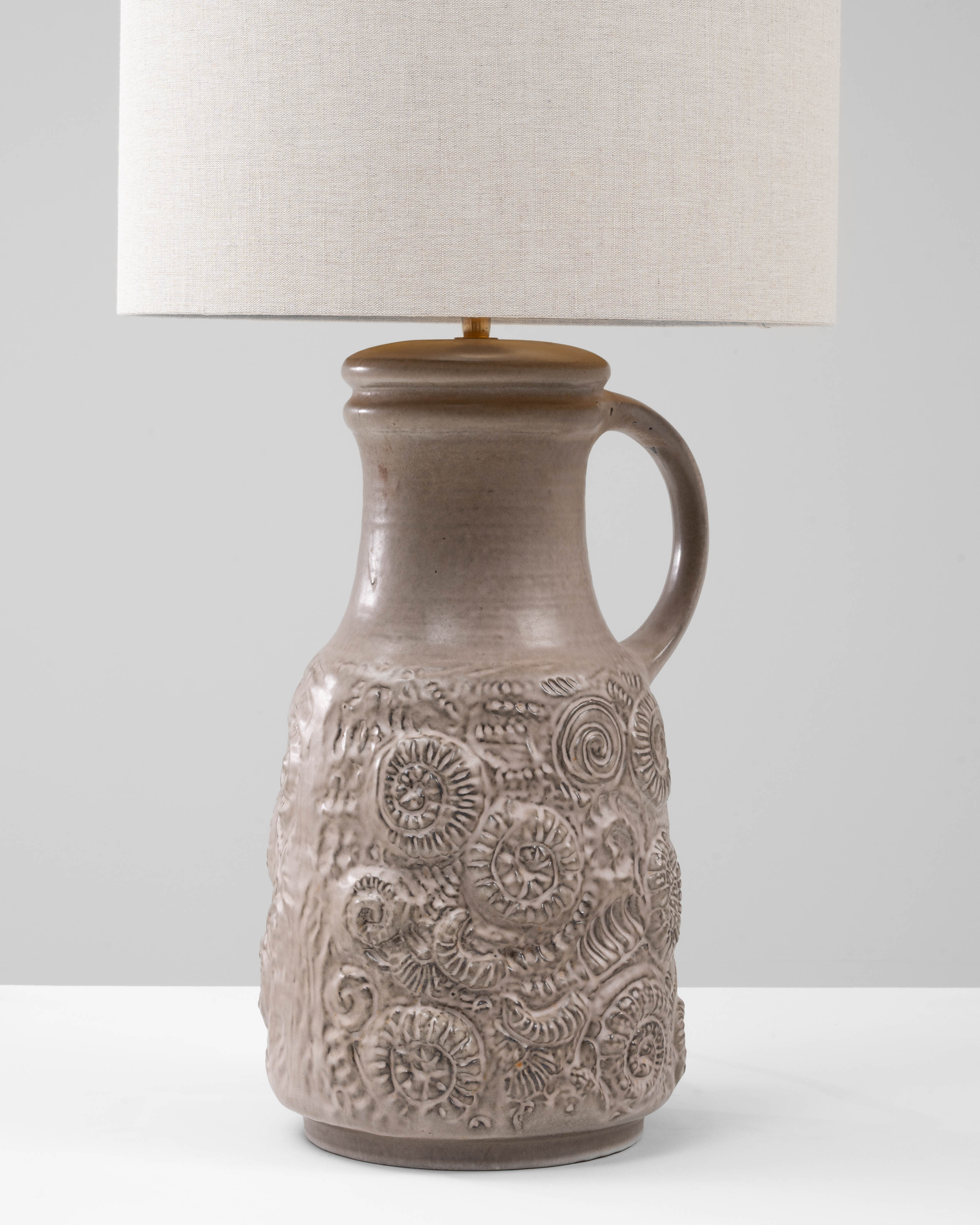 Cette lampe de table sculptée en céramique allemande du XXe siècle présente une surface expressive et richement texturée qui met en valeur l'art de la poterie européenne du milieu du siècle. La forme de la cruche se caractérise par une partie
