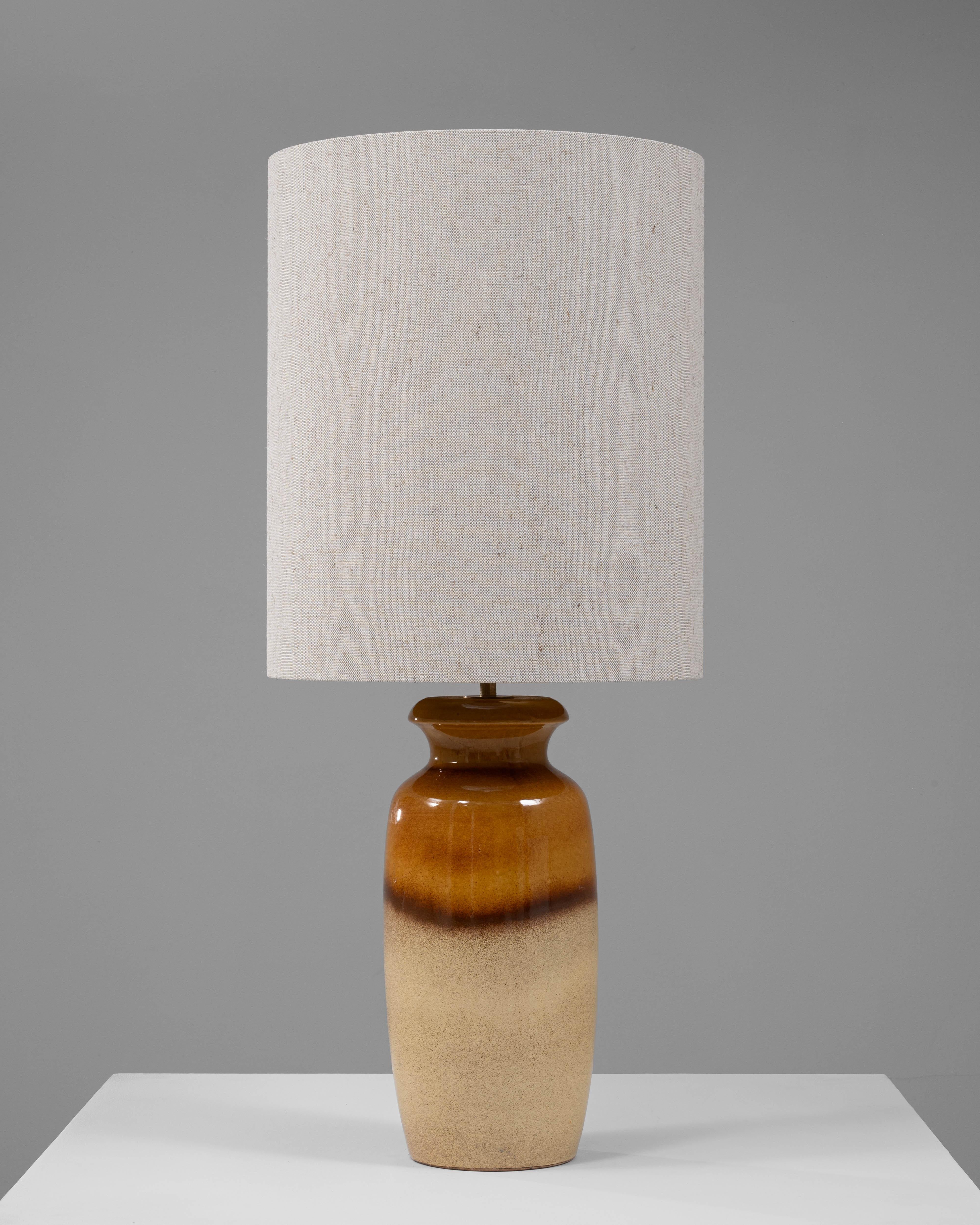 Cette lampe de table en céramique allemande du milieu du XXe siècle offre un mélange frappant de simplicité et de style. Doté d'une base en céramique émaillée avec un riche dégradé de tons chauds ambrés et beiges, il dégage un charme intemporel. Le