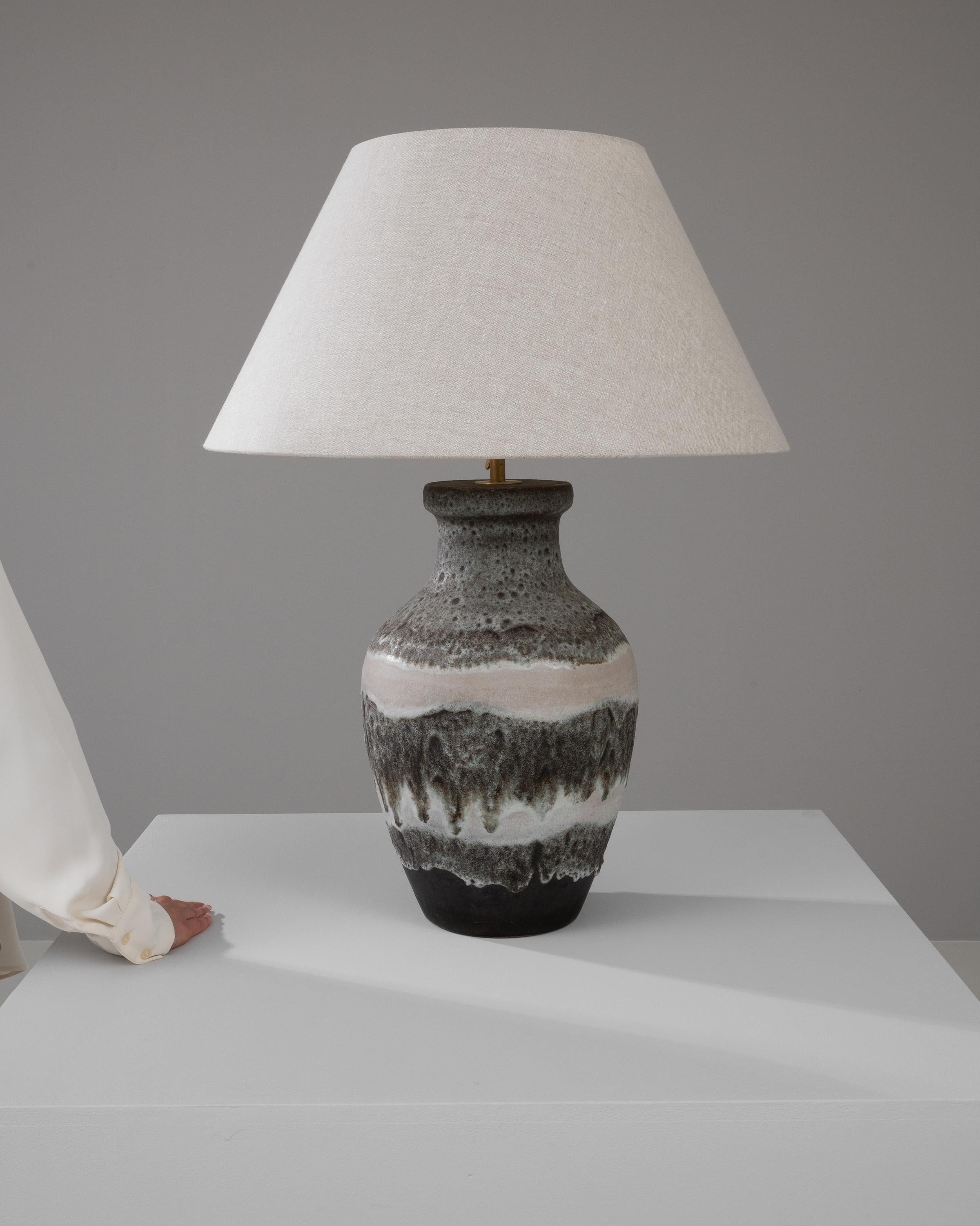 Cast a warm glow in your living space with this 20th Century German Ceramic Table Lamp, a piece where functionality meets art. Its stout, earthy ceramic base is a canvas of abstract beauty, with a speckled glaze that cascades over the robust form,