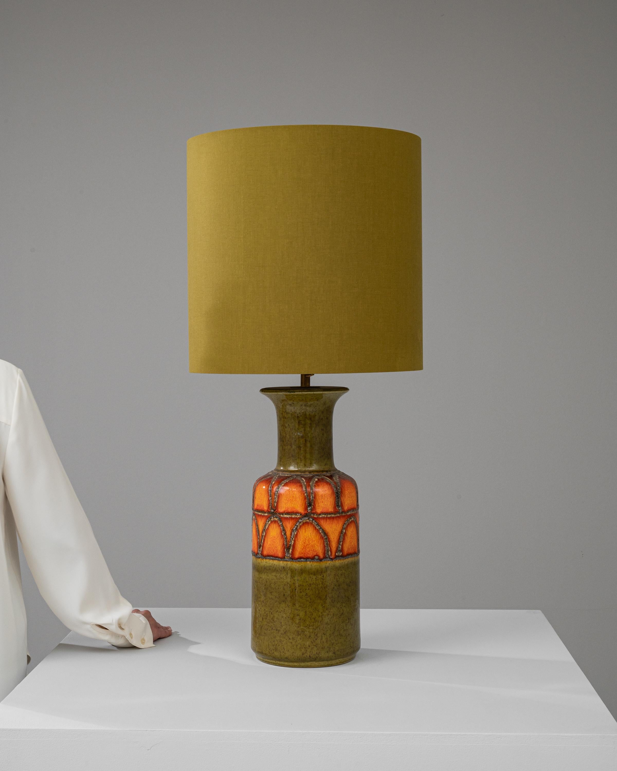 Elevate your home decor with the vibrant allure of this 20th Century German Ceramic Table Lamp, a true emblem of retro-chic style. The lamp's base captivates with its bold, fiery orange hue set against an organic olive background, creating a
