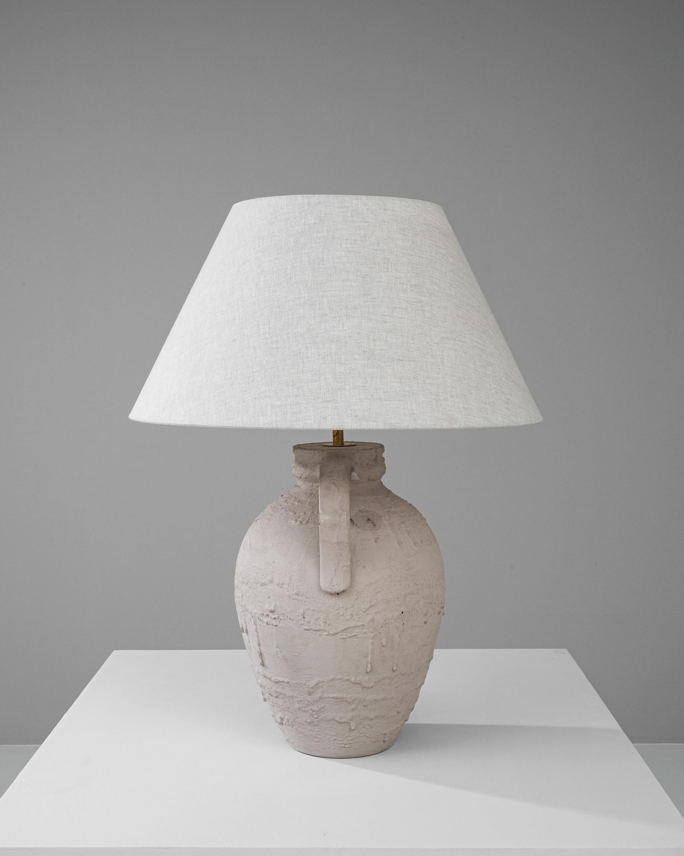 This 20th Century German Ceramic Table Lamp offers a pure and elemental aesthetic that evokes a sense of serene, rustic charm. Its stout, textured base is reminiscent of ancient pottery, carrying the marks and nuances of traditional craftsmanship.