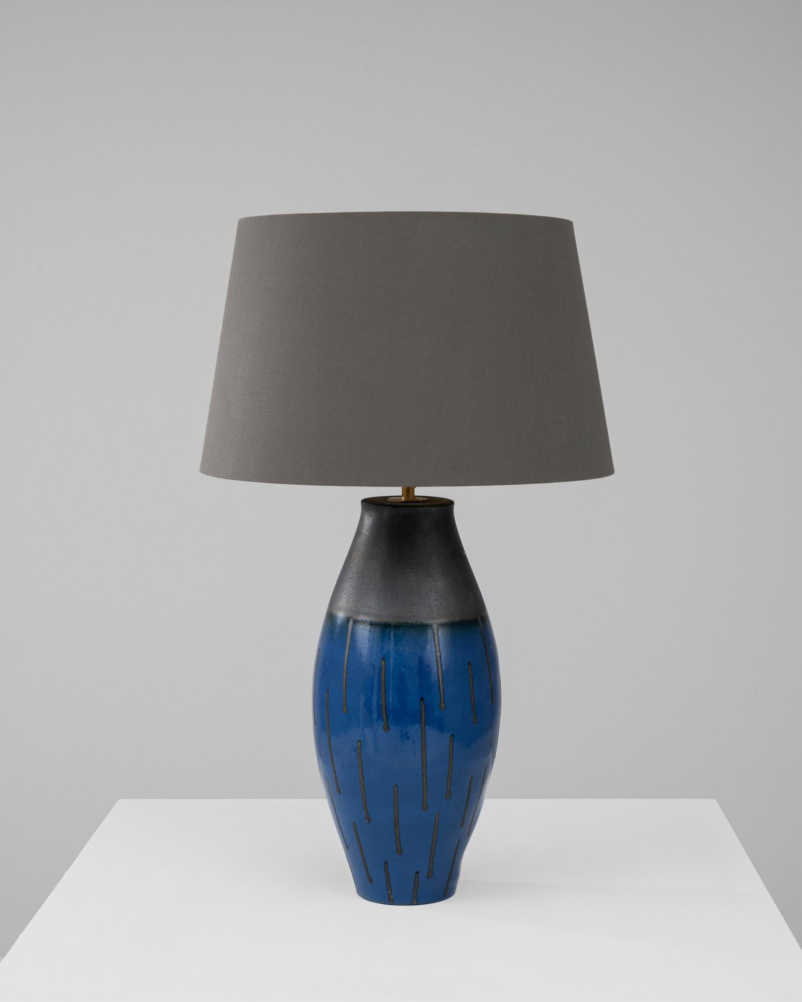 Illuminate your space with the captivating aura of the 20th Century German Ceramic Table Lamp, a masterpiece of both form and function. This striking lamp boasts a vivid, cobalt blue ceramic base with a gracefully tapered form, accented with bold,